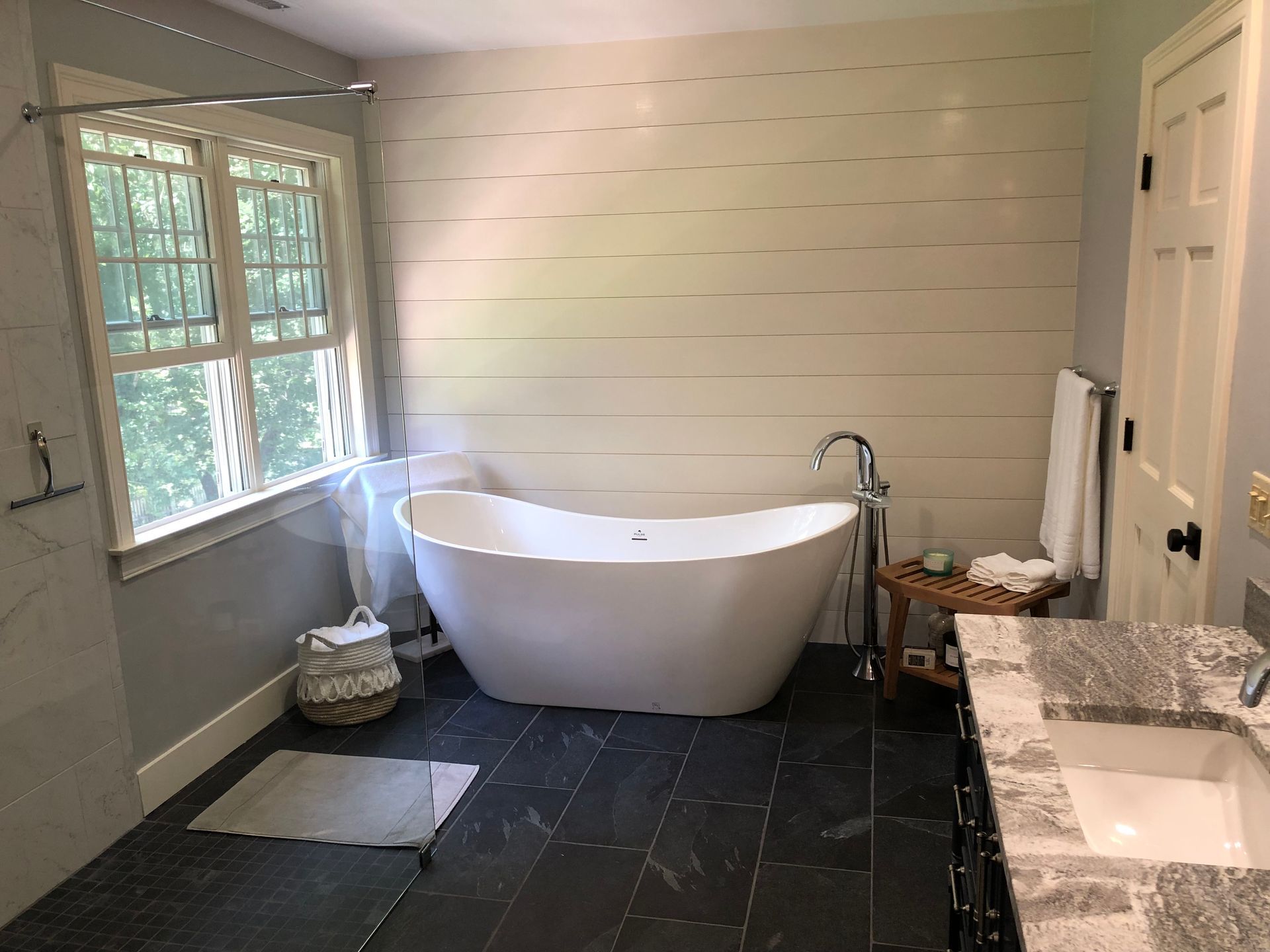 Bright bathroom with freestanding tub, double sinks, dark tile floor, and large window by the tub