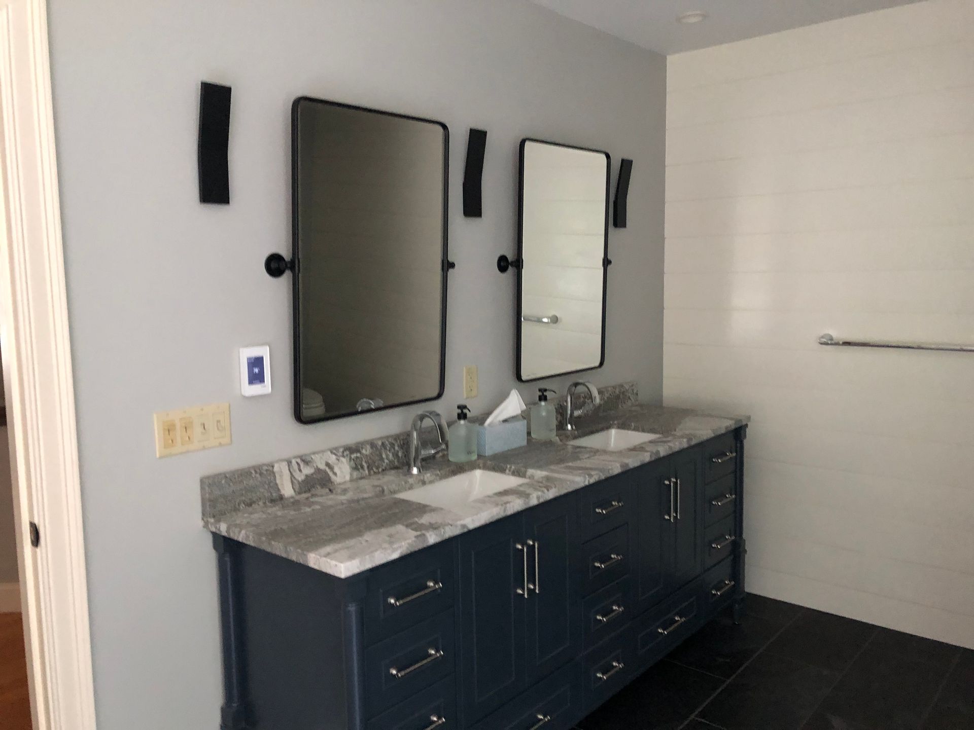 Modern bathroom vanity with double mirrors, dark cabinets, gray countertop, and wall-mounted lighting