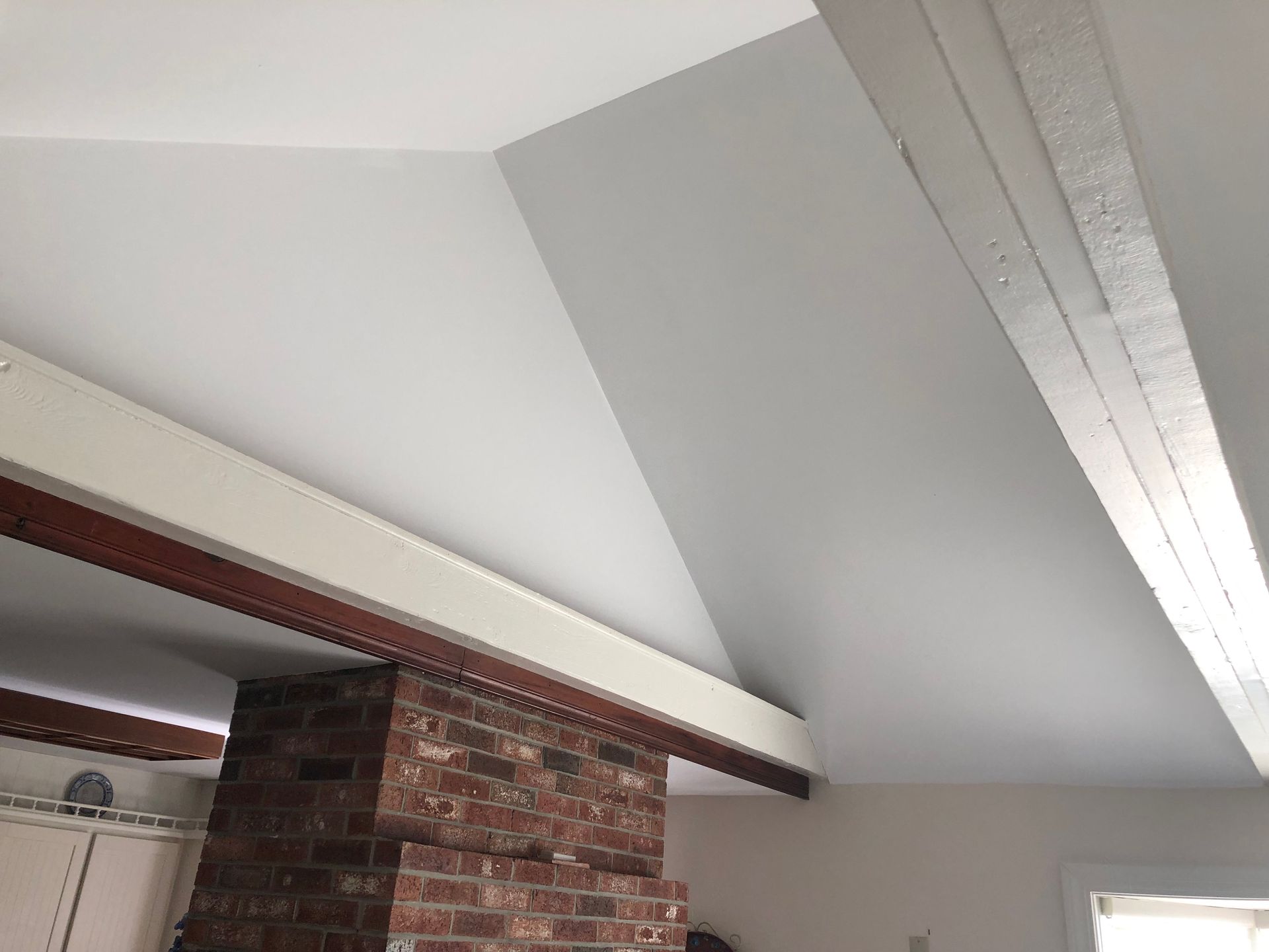 Sloped white ceiling with exposed brick chimney and wooden beam in a room corner