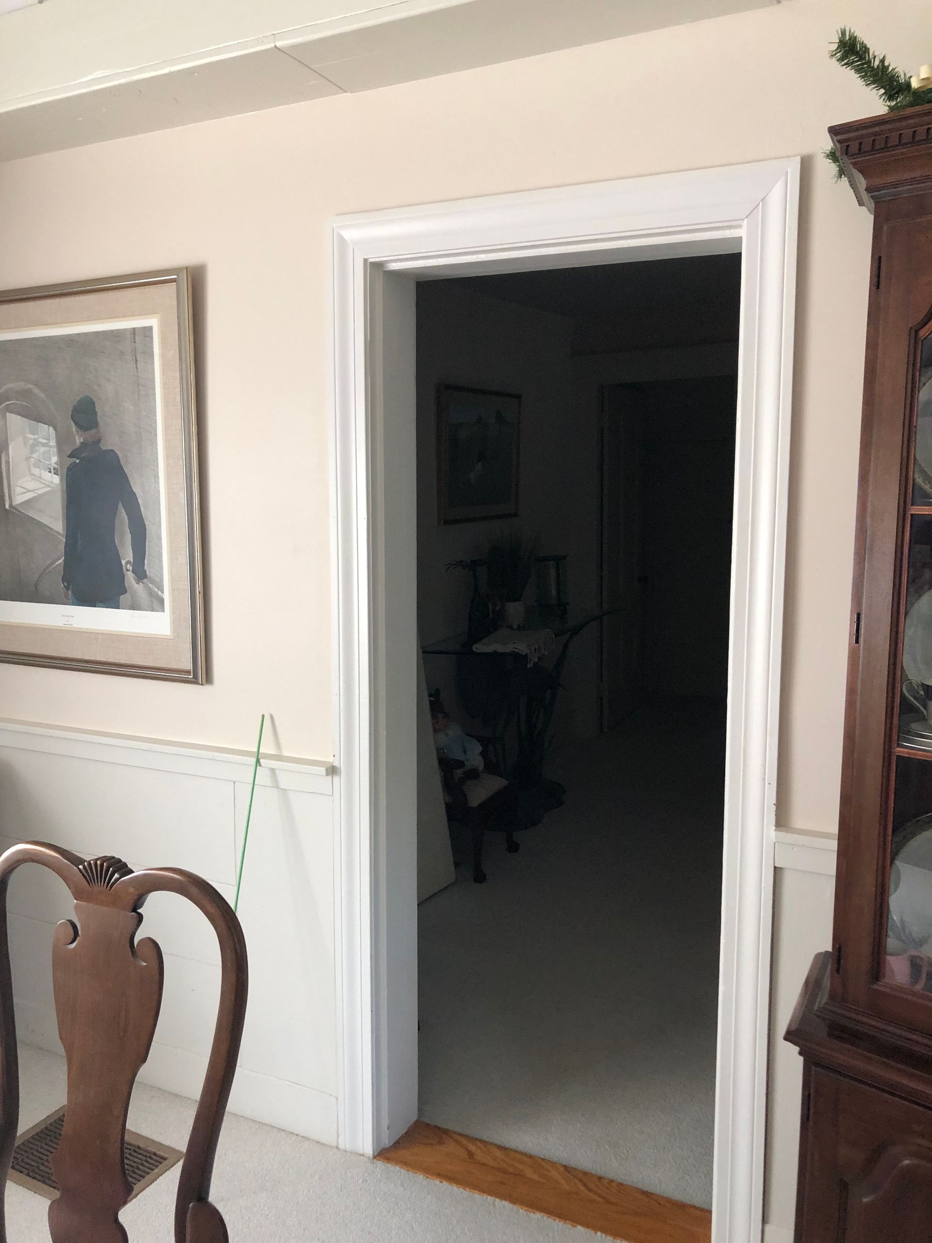 Living room with open doorway into a dark hallway, framed art on the wall and a wooden chair in the foreground