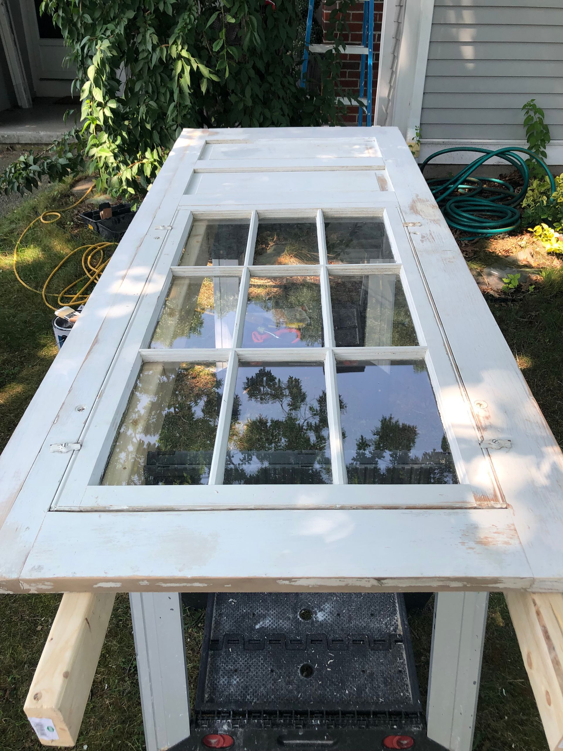 Old white door with glass panes laid across sawhorses outdoors in a yard