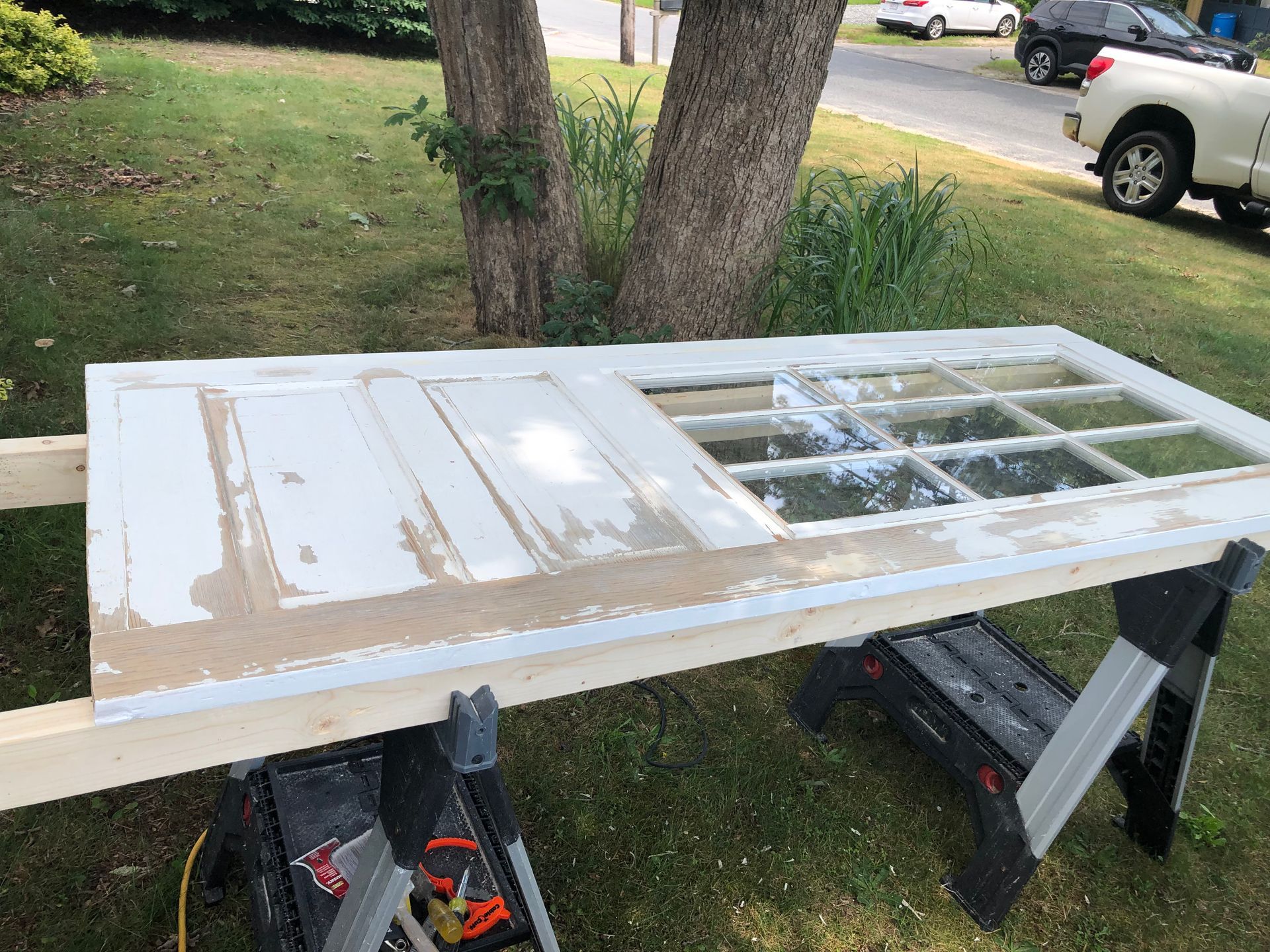 White door laid across sawhorses outdoors beside a window screen, with a driveway and truck in the background