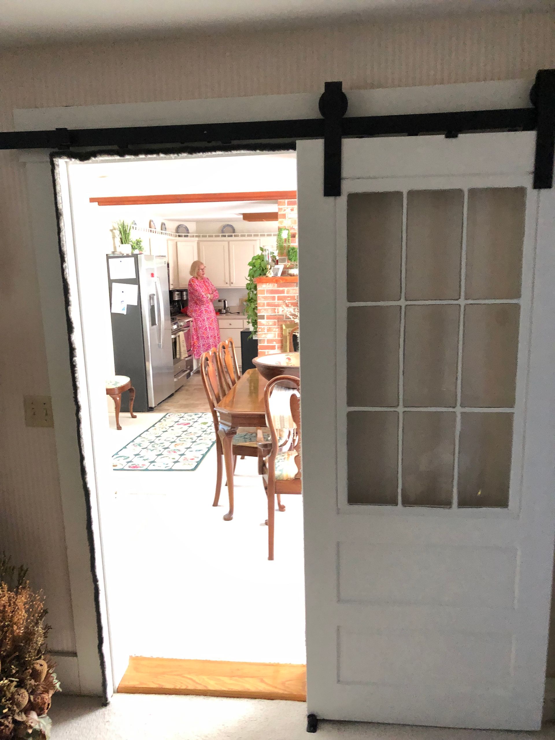 Open white door to a bright kitchen with a person in pink standing near the table.