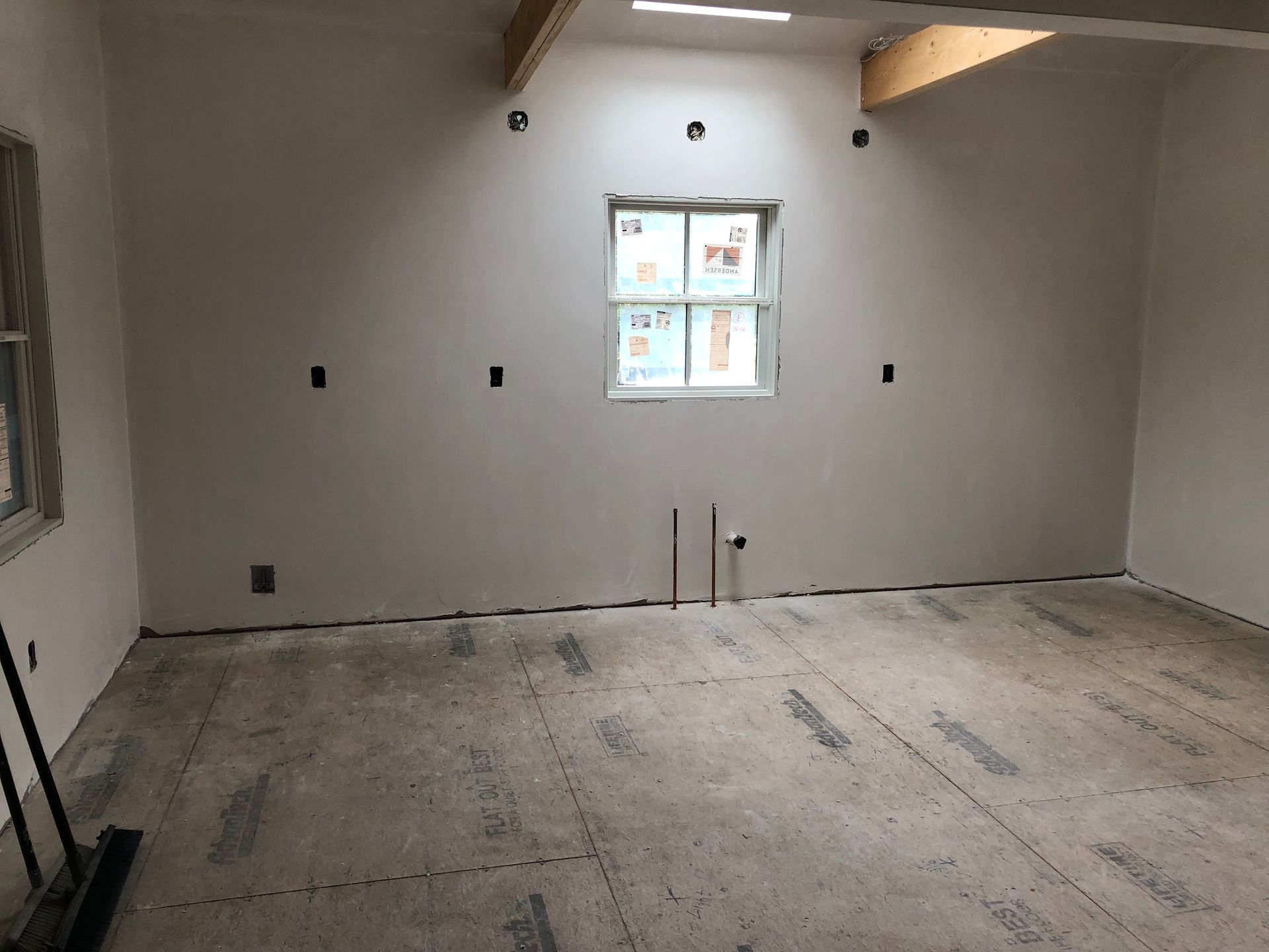 Empty room under renovation with unfinished floor, white walls, and a small window