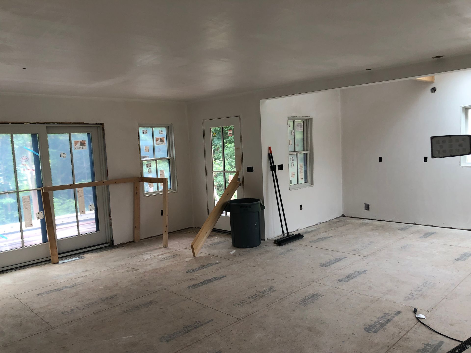 Empty unfinished room with white walls, windows, tools, and construction materials on the floor.