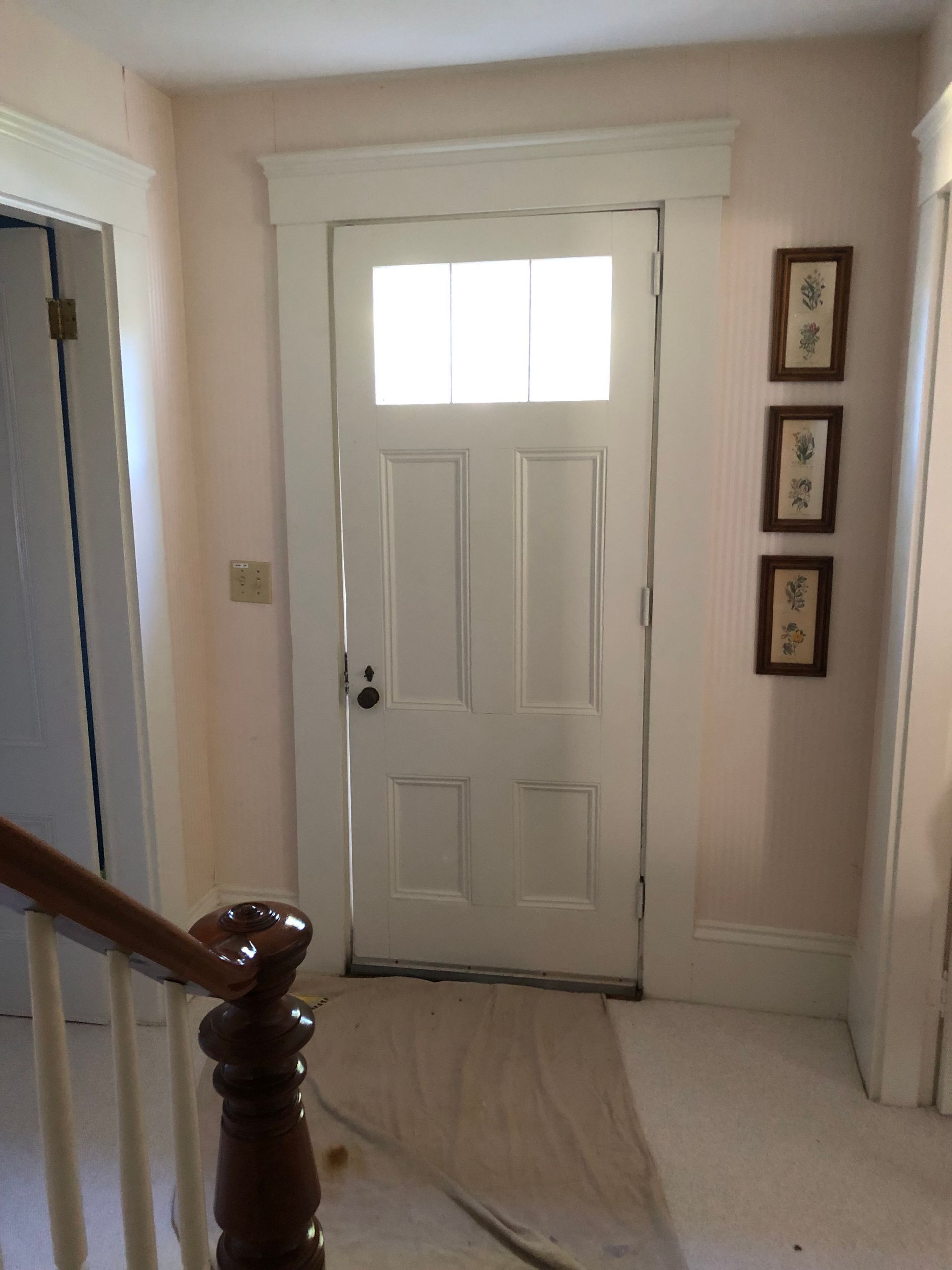 White front door with sidelights in a beige hallway, beside a staircase and framed wall art.