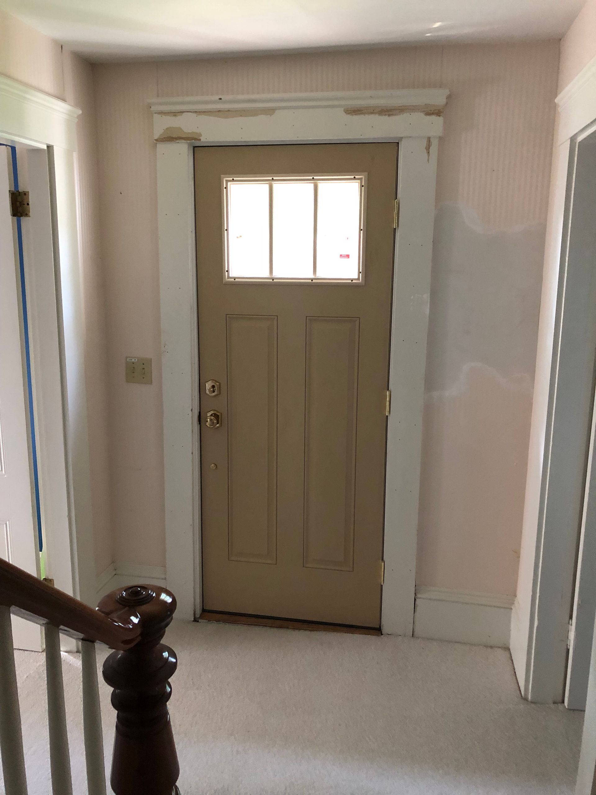 Hallway with a beige front door, white trim, and a partially painted wall under renovation