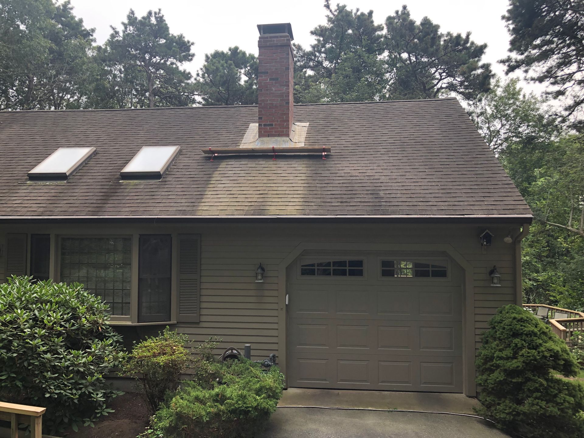 Suburban house exterior with skylights, chimney, and attached garage surrounded by trees