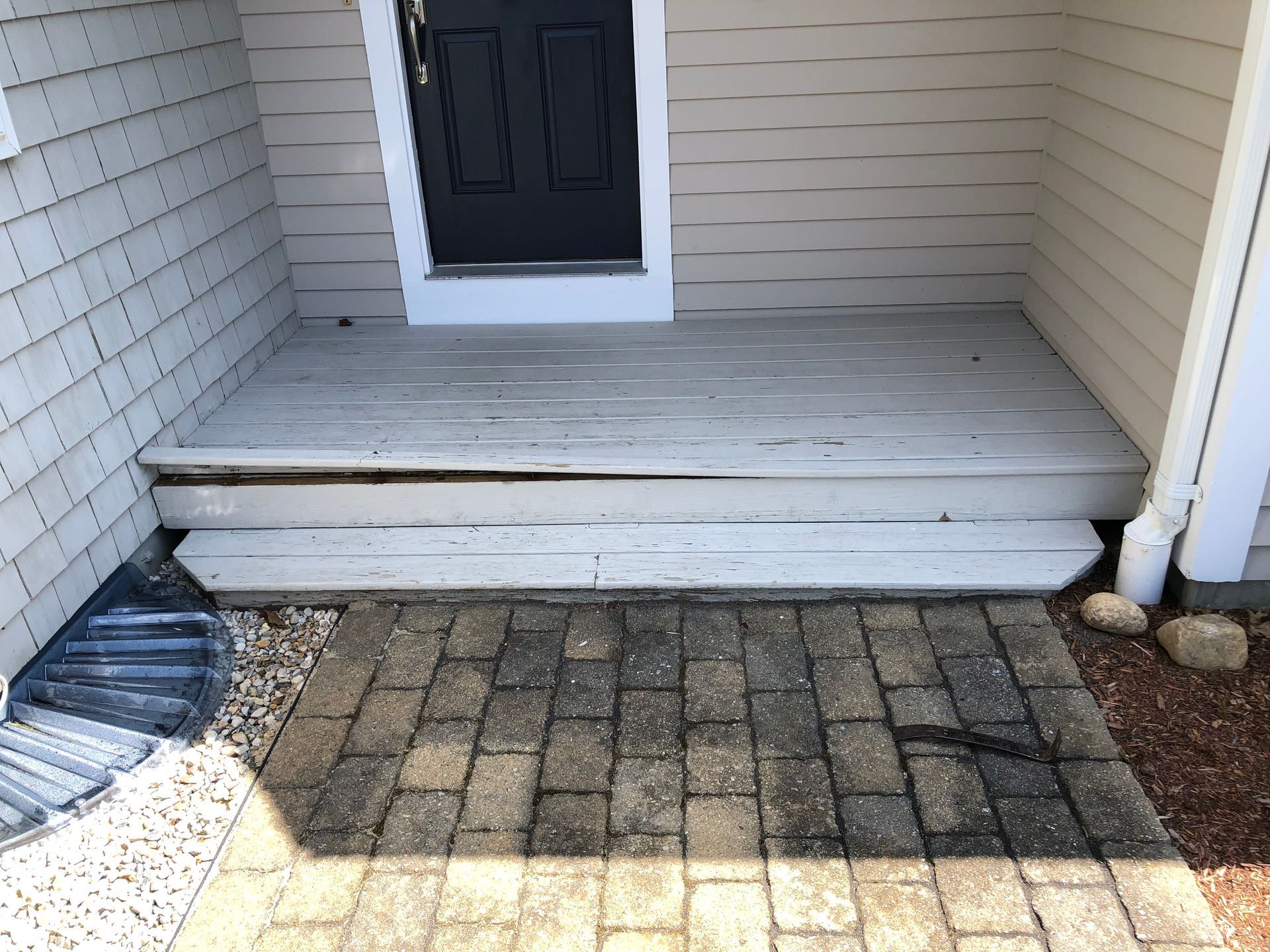 Front porch with a short step, black door, and brick walkway leading to the entryway