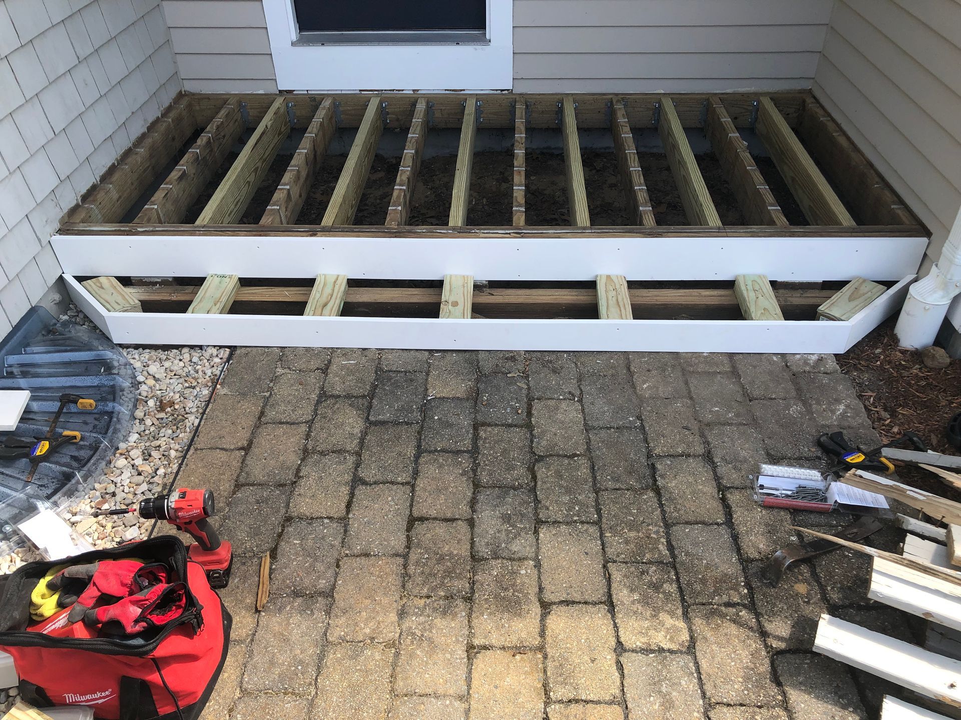 Partially built porch deck with exposed joists and scattered tools in front of a house