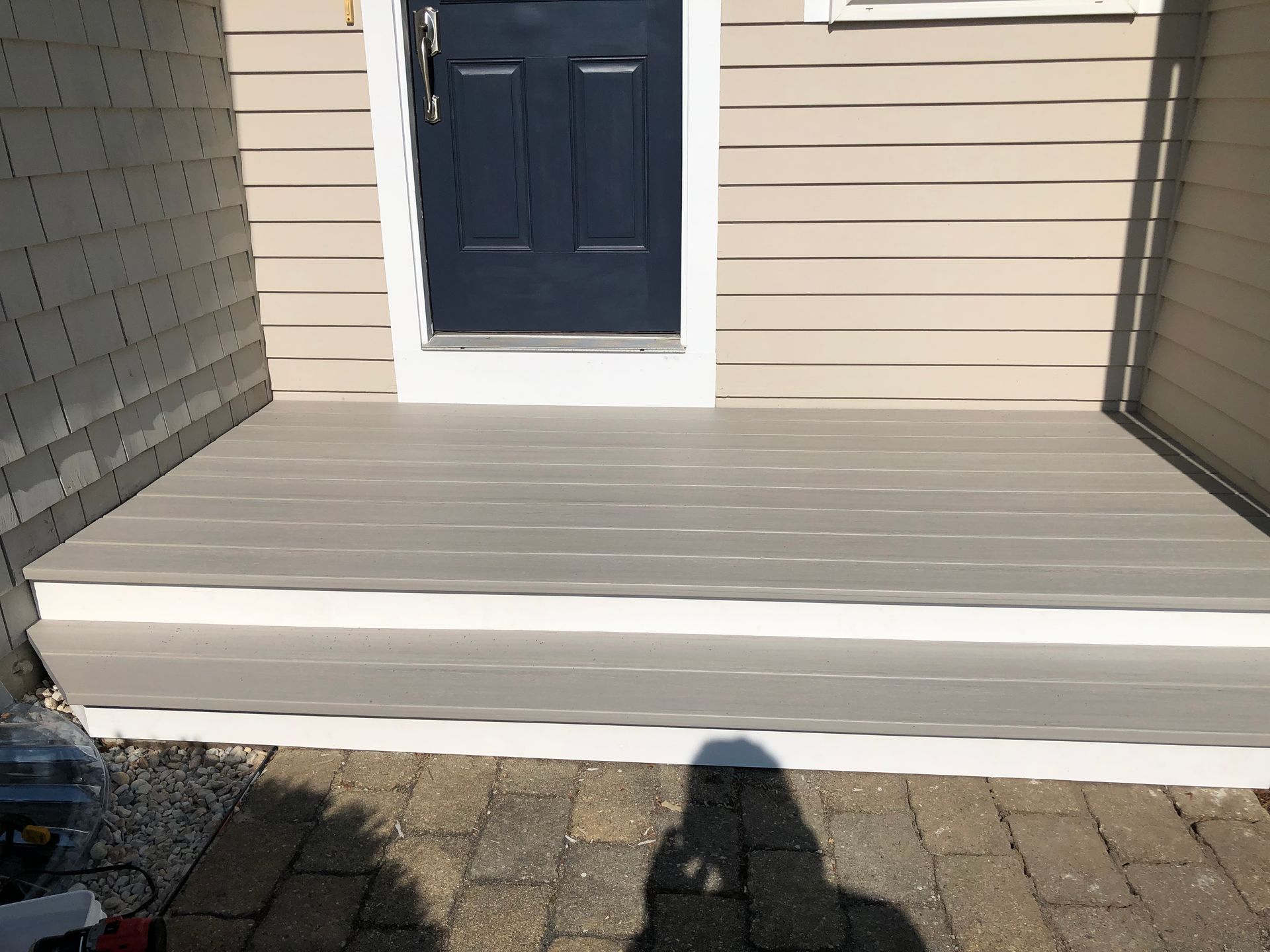 Front porch with light gray deck and dark blue door, viewed from a brick patio.
