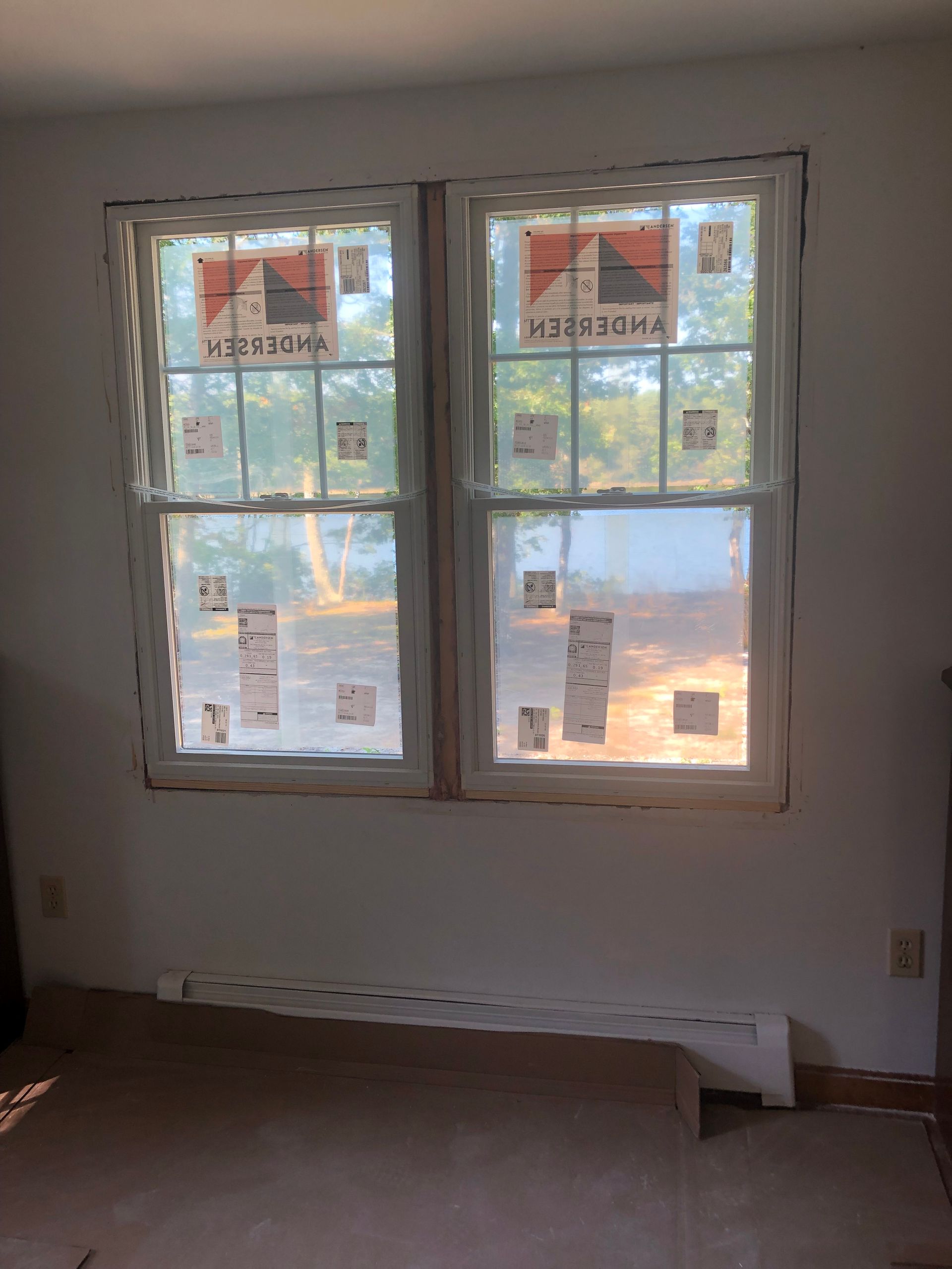 Bare room with two windows, bare floor, and daylight filtering in through closed blinds or taped covering.