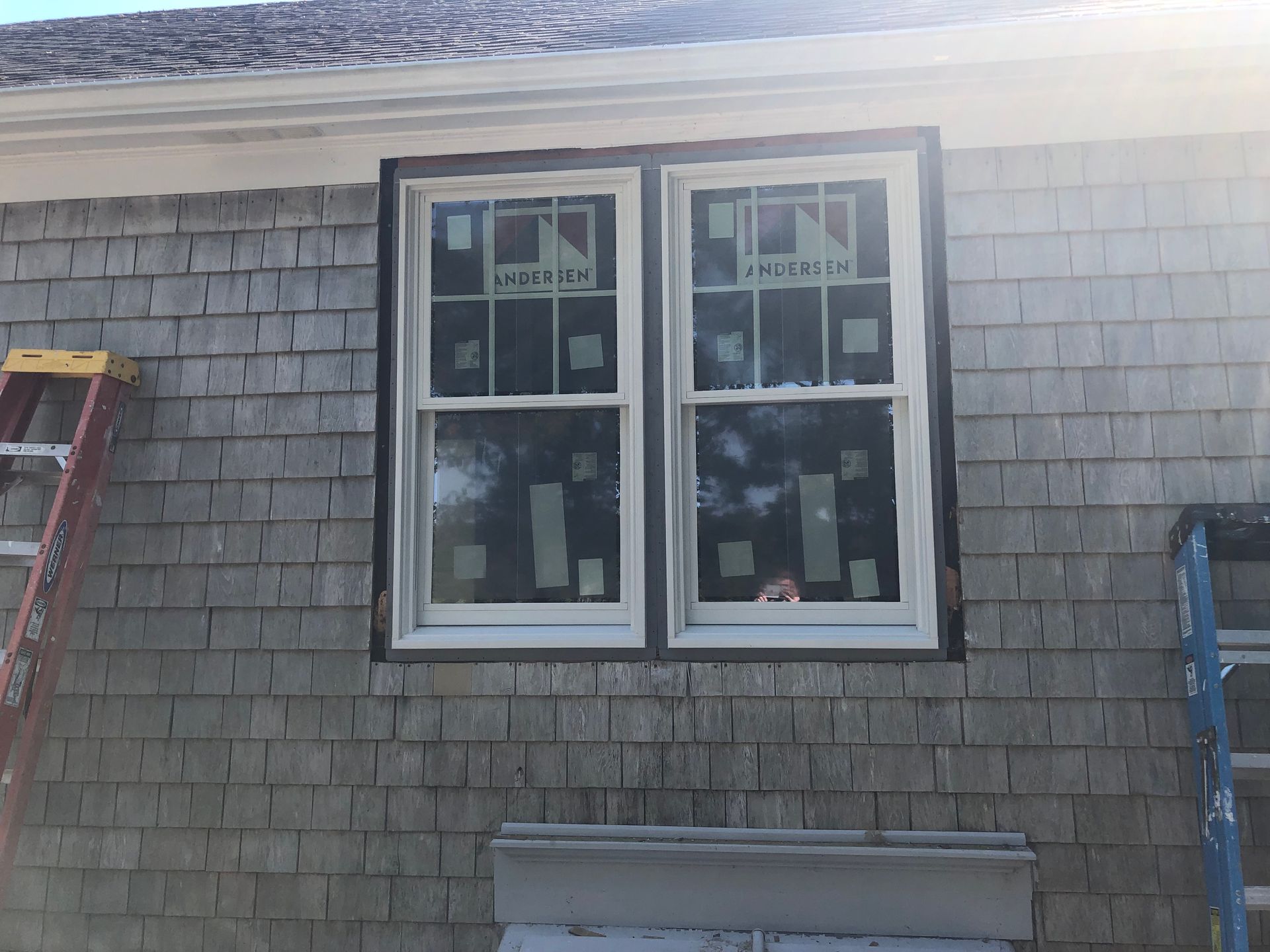 House exterior with two white-trimmed windows and gray shingle siding, ladder visible at the sides