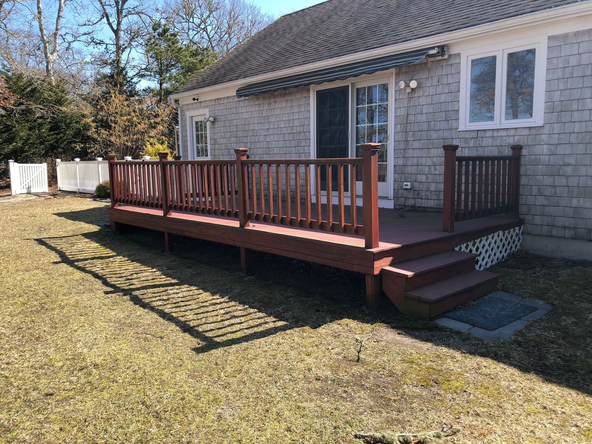 Stone house with a red wooden deck and stairs in a grassy yard, with laundry hanging nearby