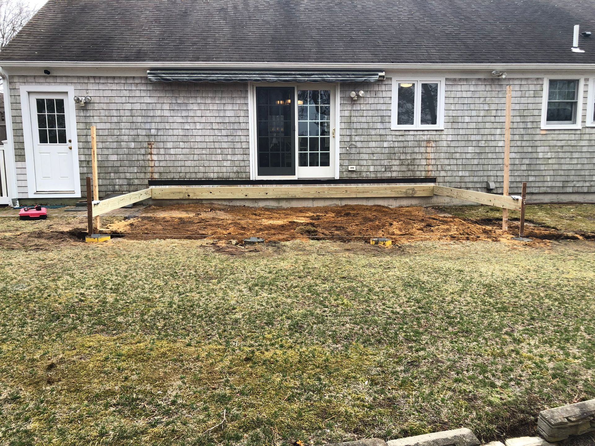 Weathered house exterior with a small front porch under construction and bare yard