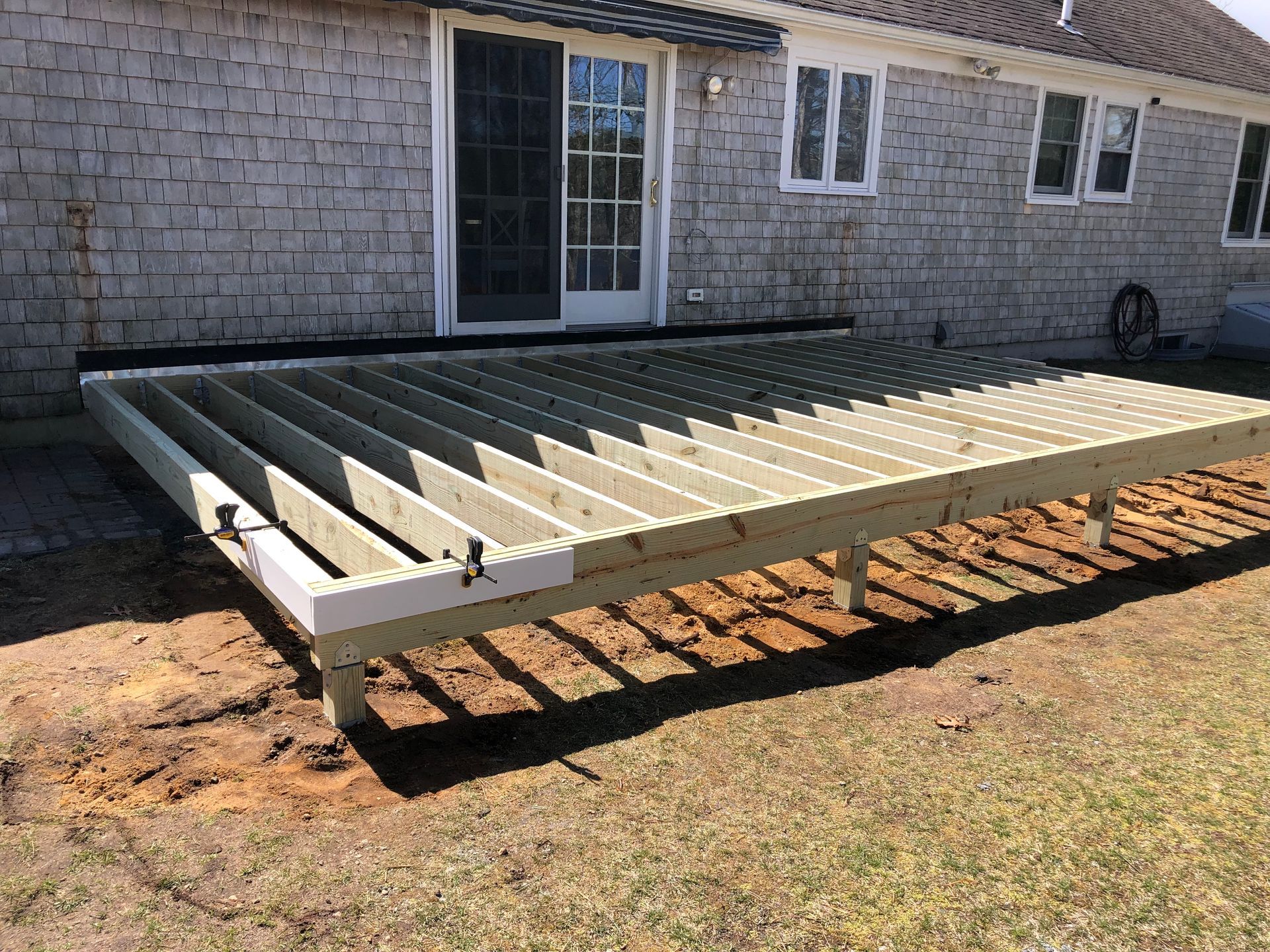 Raised wooden deck frame under construction beside a house, with exposed joists and beams.