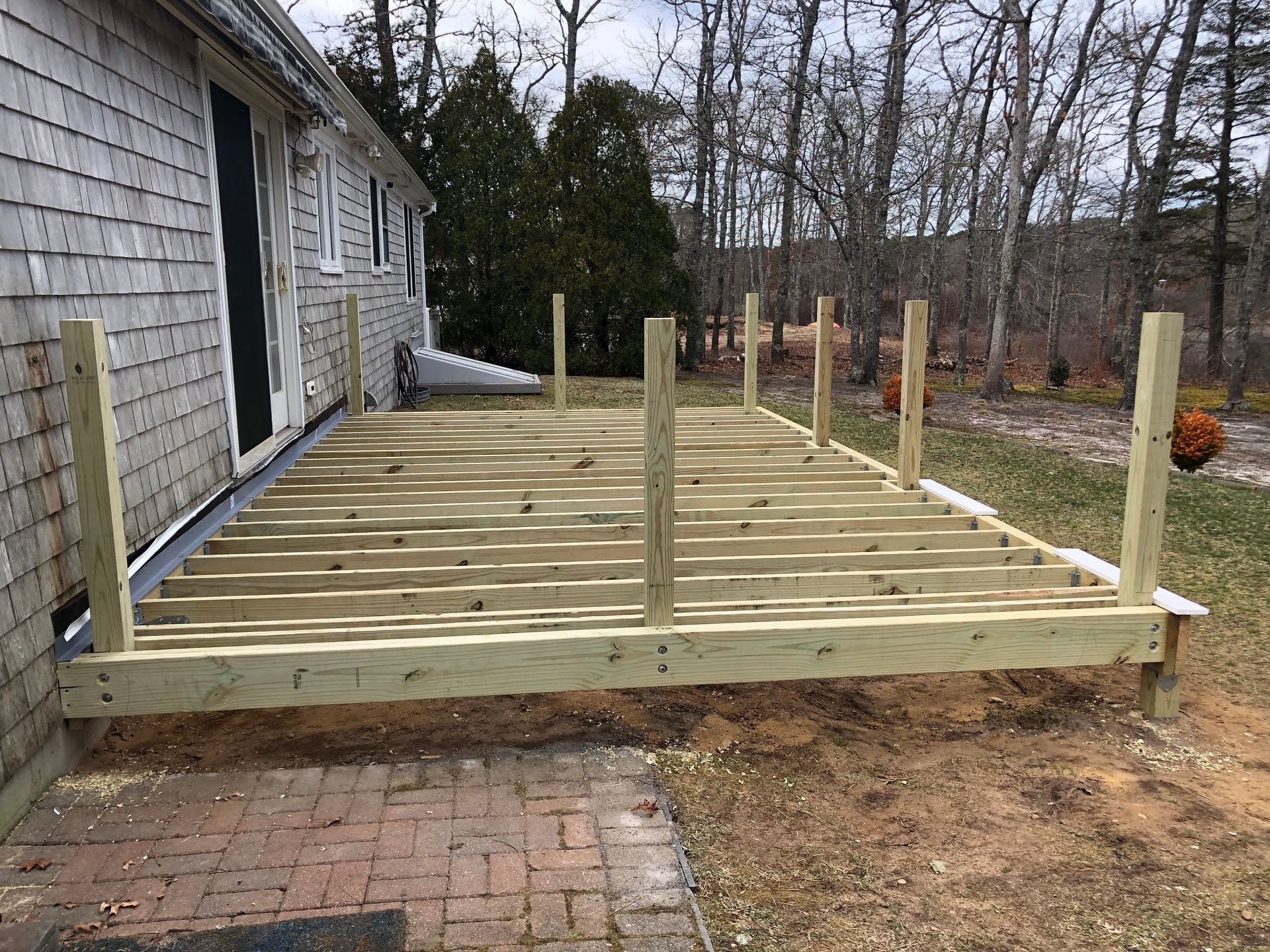 Wooden deck frame under construction beside a house, with brick steps and support posts.
