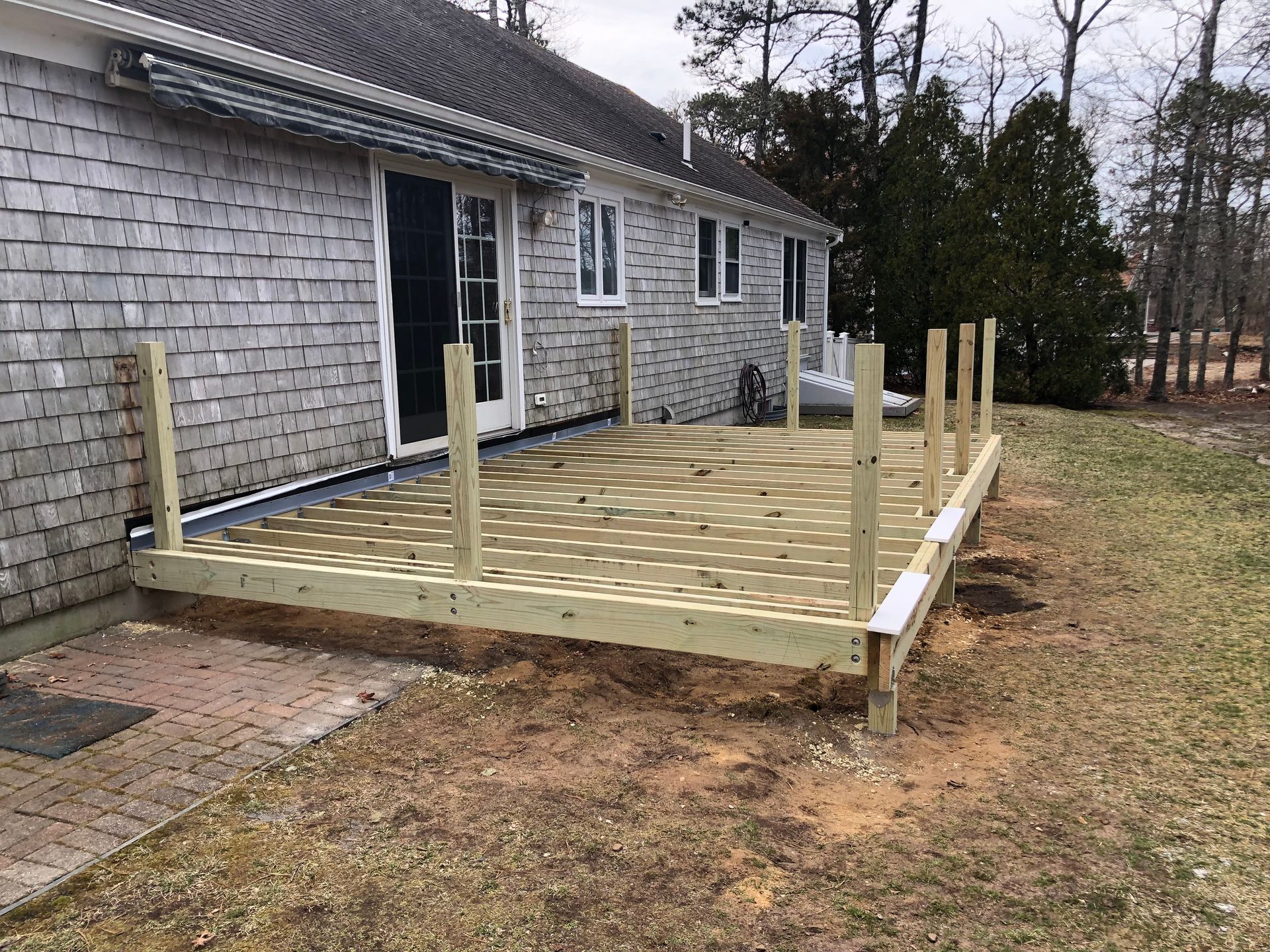 Wooden deck frame under construction beside a gray house with several vertical posts and unfinished boards