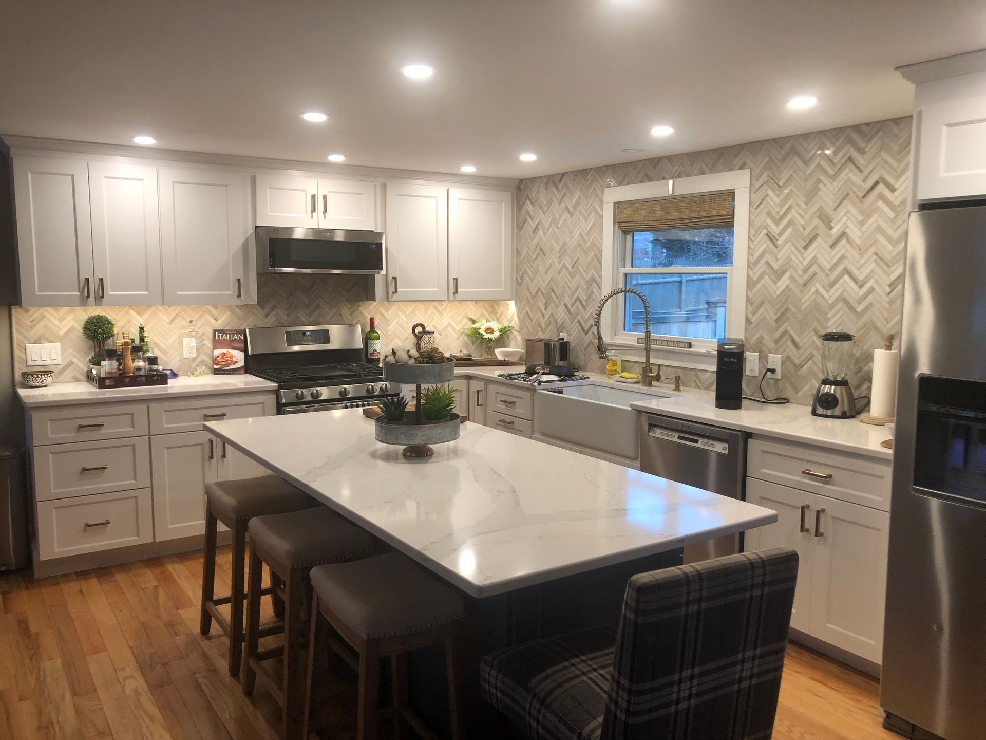 Bright modern kitchen with white cabinets, island, stainless appliances, and herringbone tile backsplash