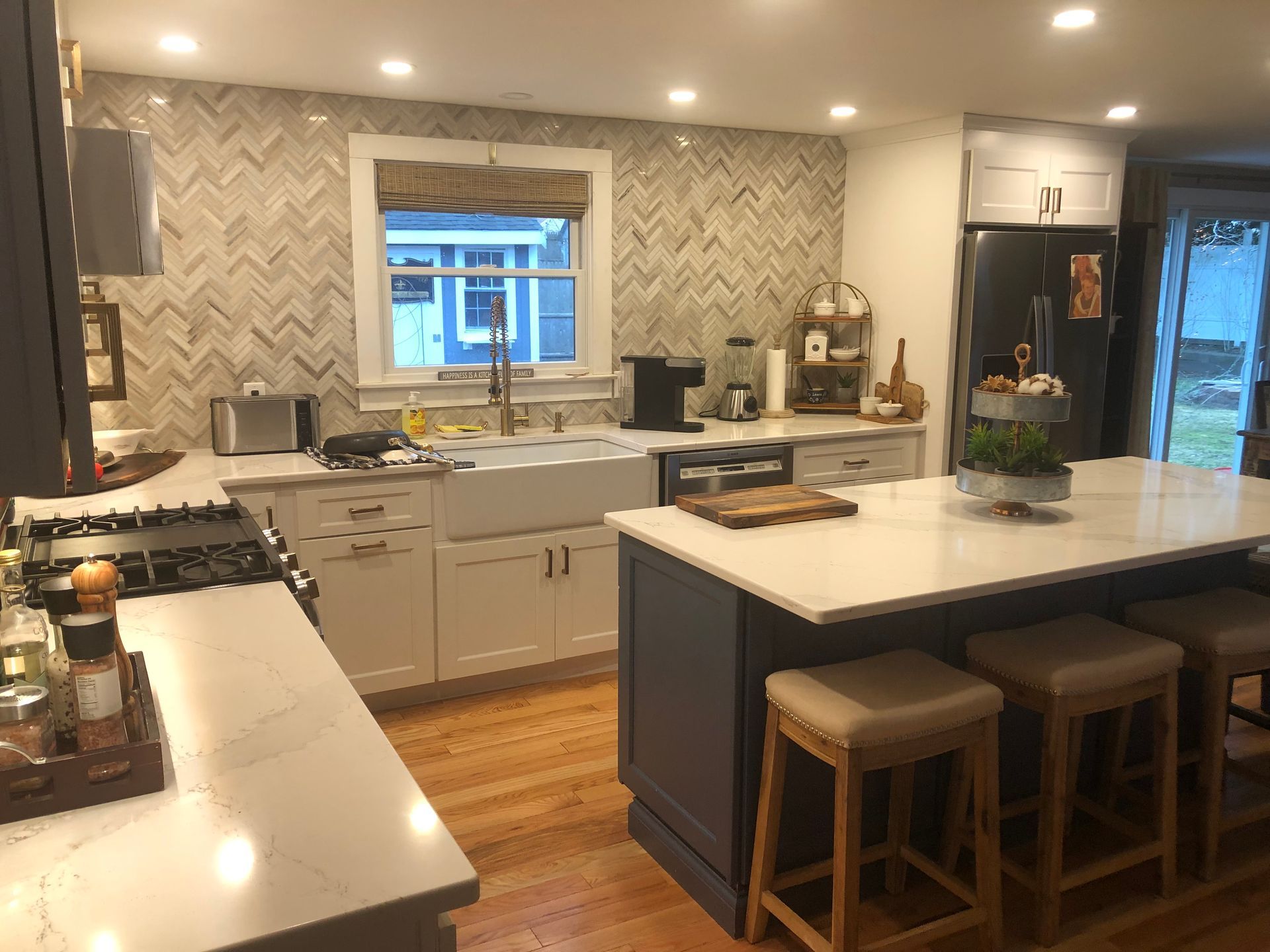 Modern kitchen with white island, gray cabinets, wood floor, and a window above the sink