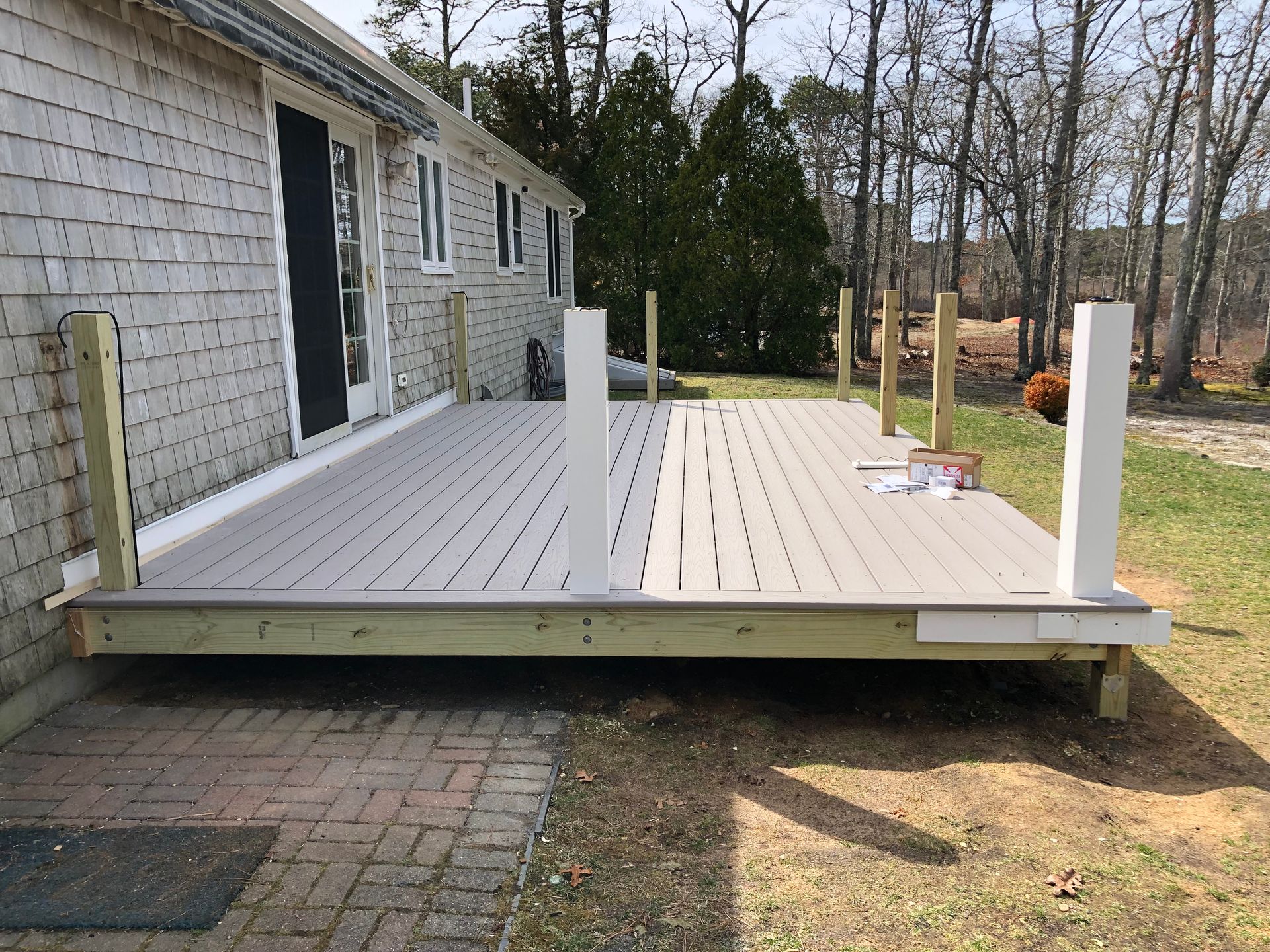 Front porch deck under construction beside a house, with white rail posts and gray decking boards.