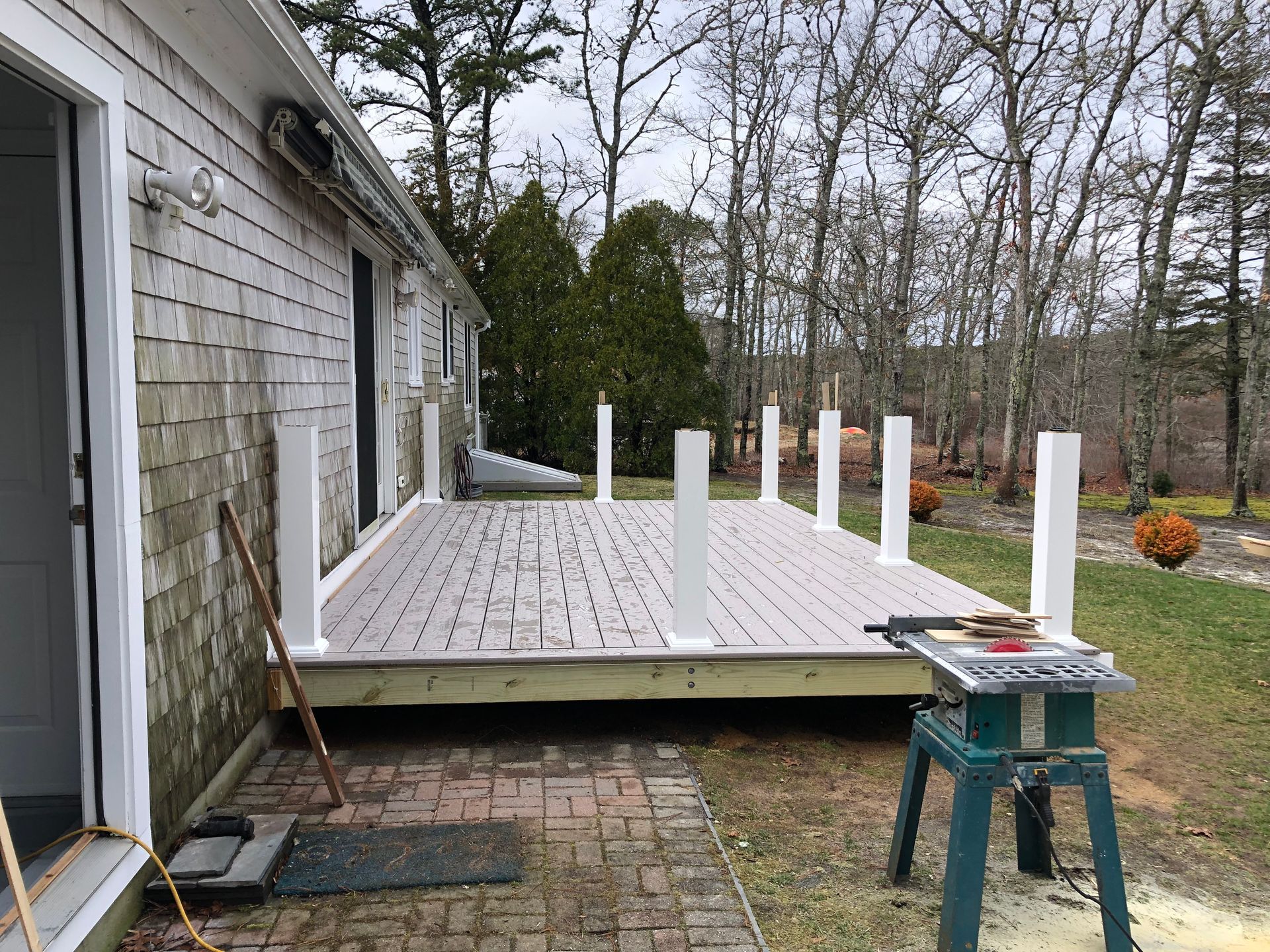 Partially built wooden deck beside a house, with white support posts and tools on a small stool.