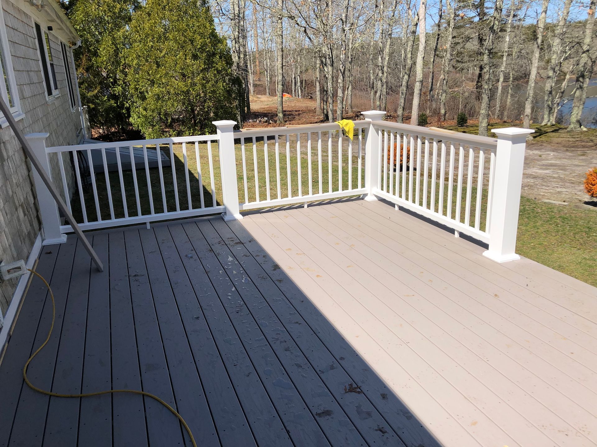 Wooden deck with white railing beside a house, overlooking a yard and trees