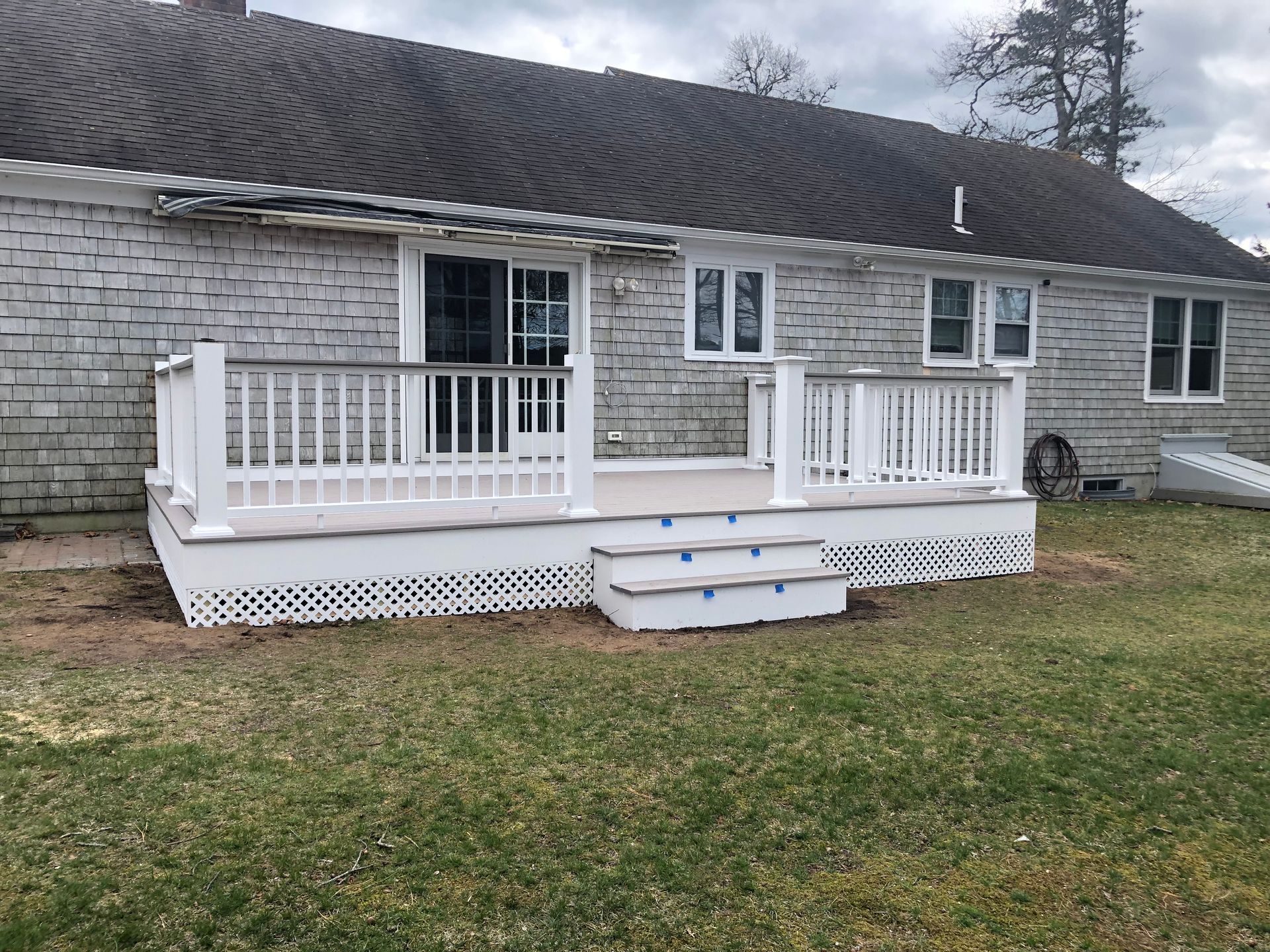 White porch deck with railings and steps on a gray brick house, viewed from the lawn