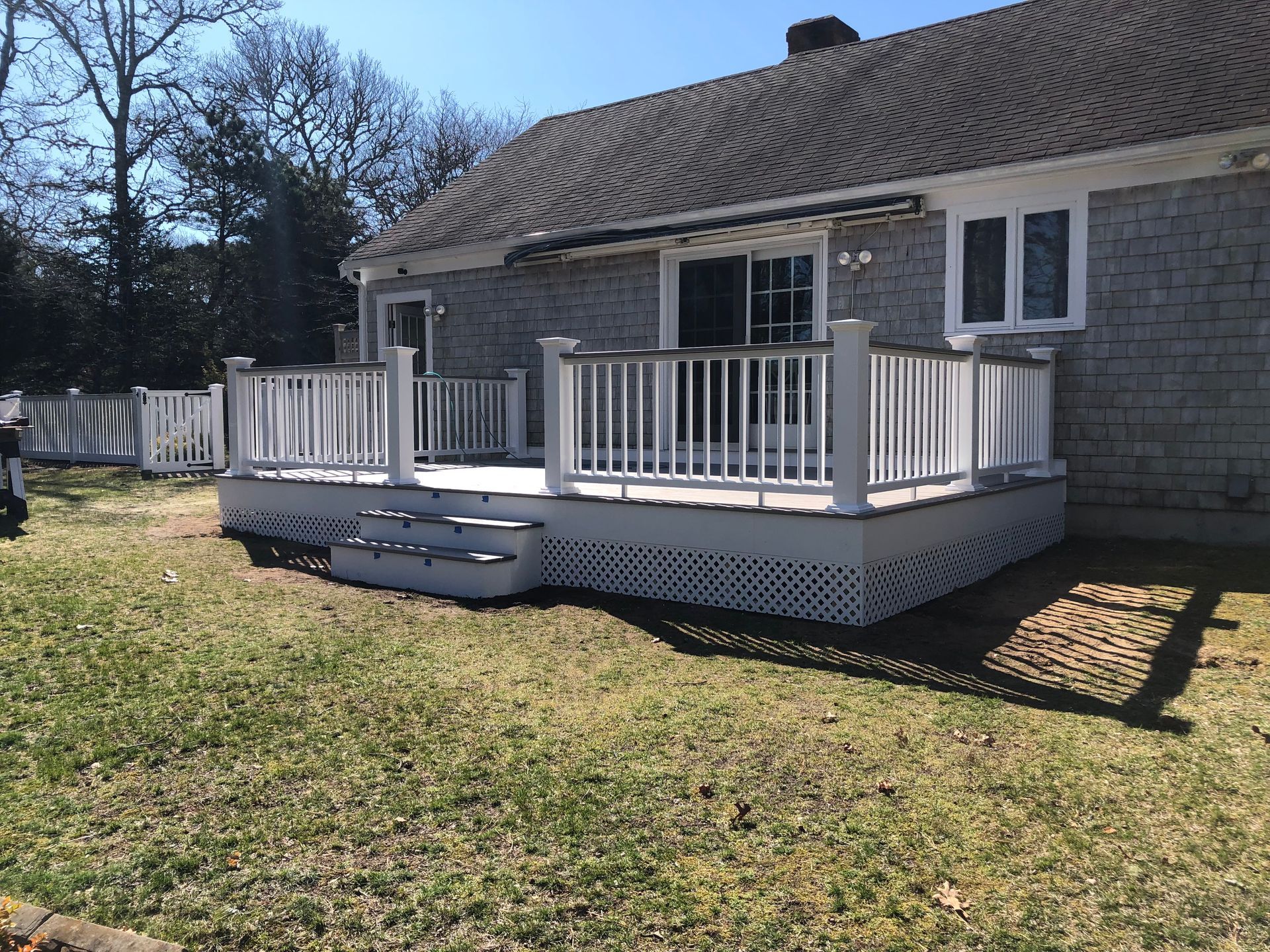 Back porch with white railings and steps attached to a gray house on a sunny day
