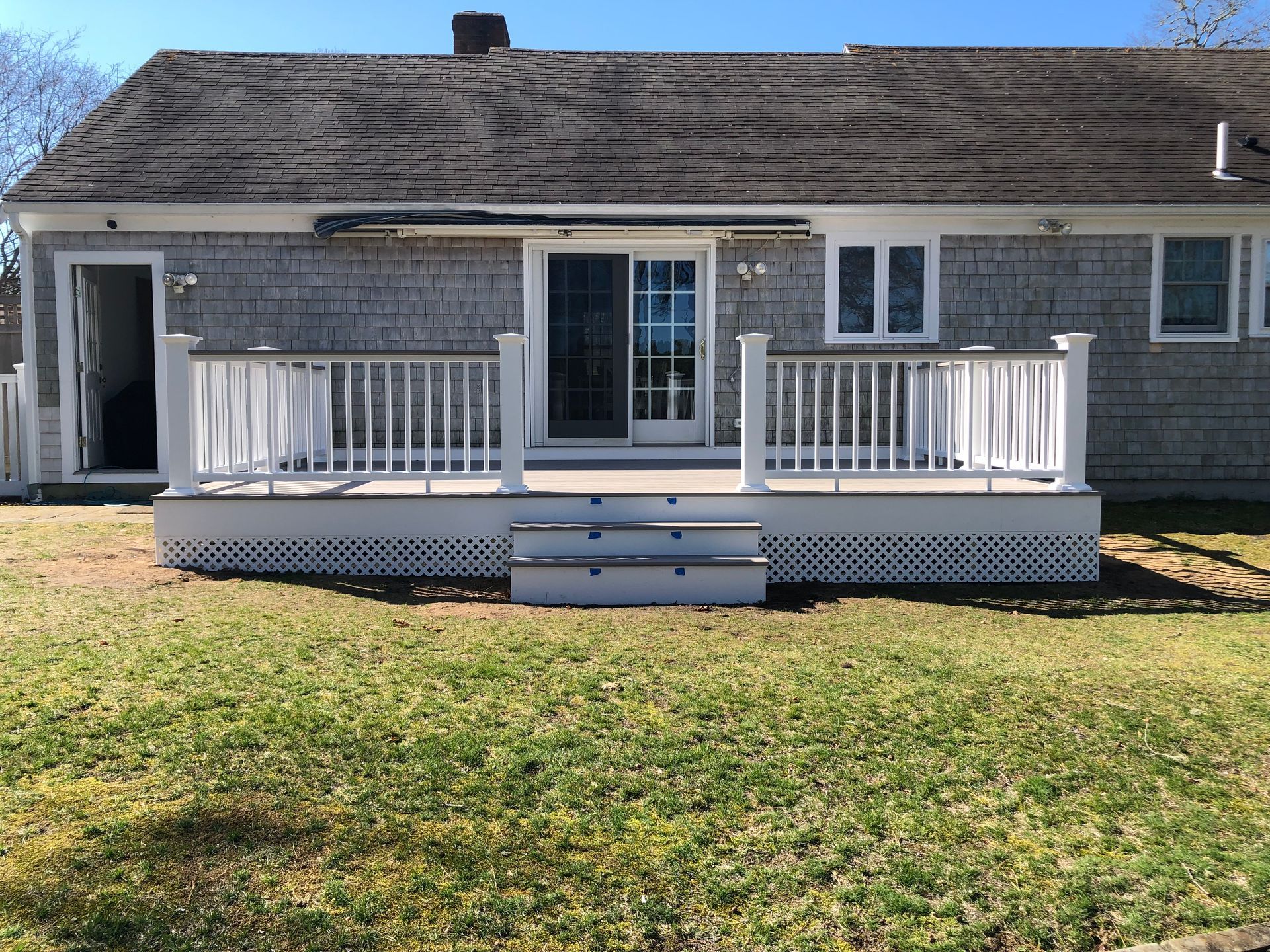 Back of a house with a white wooden deck and steps, facing a grassy yard.