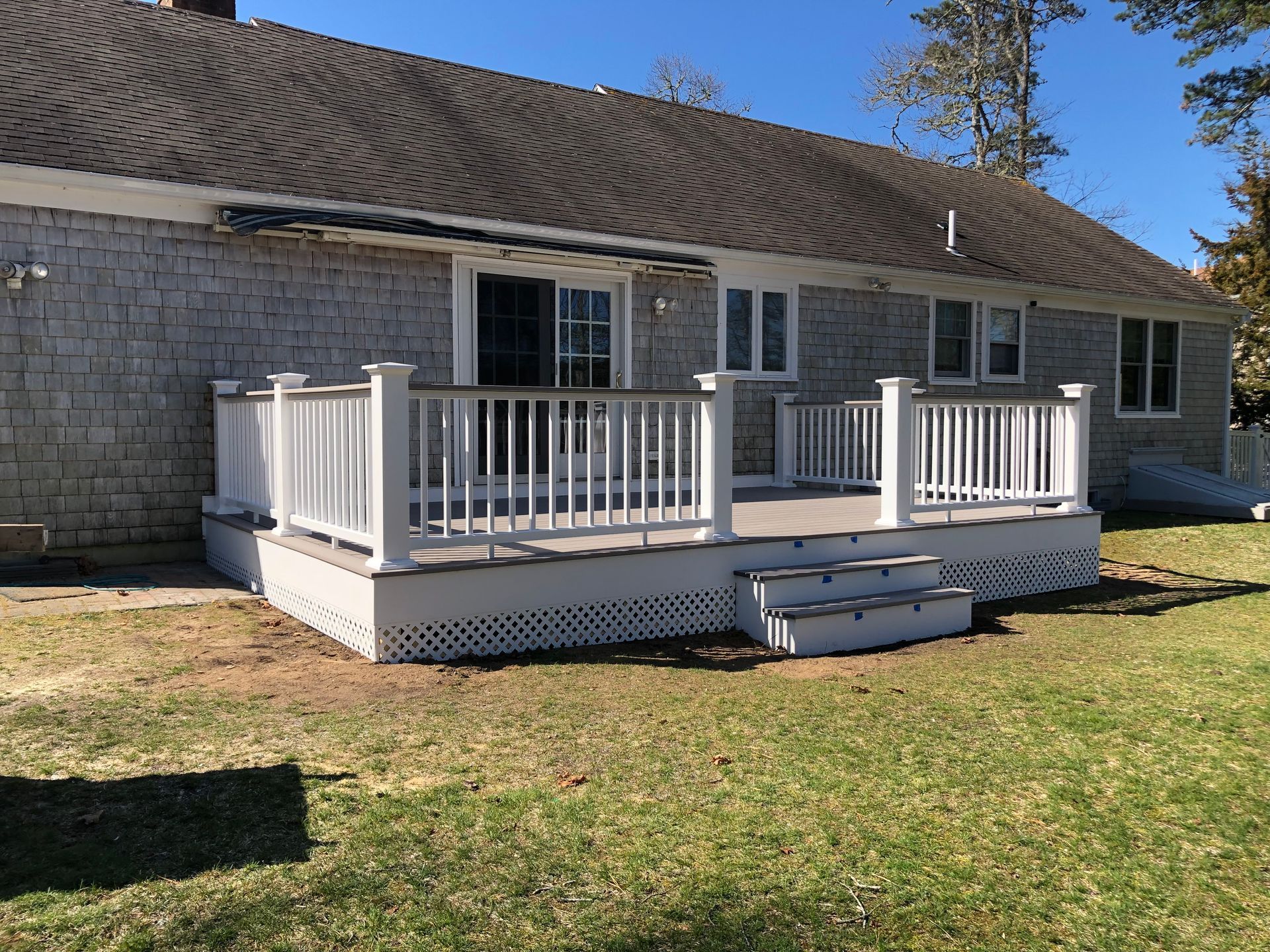 White porch deck with railings and steps attached to a stone house on a sunny day