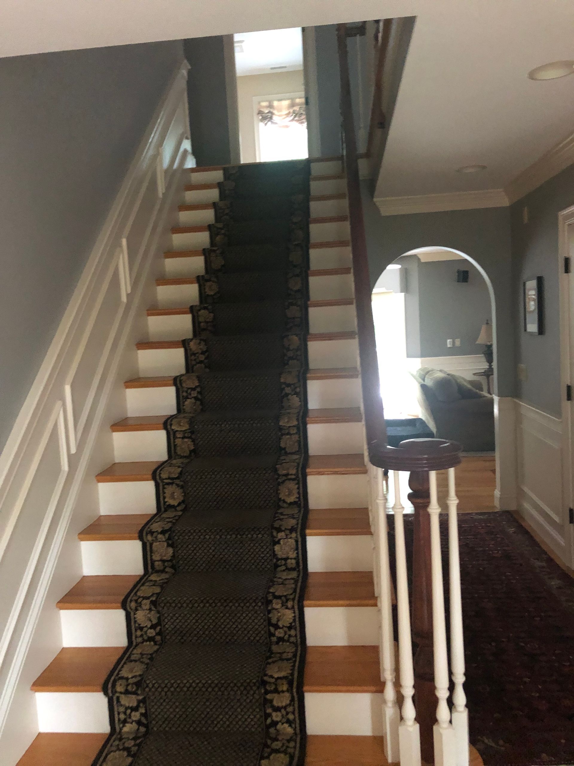 Staircase with patterned runner carpet, white banister, and arched hallway opening on the right.
