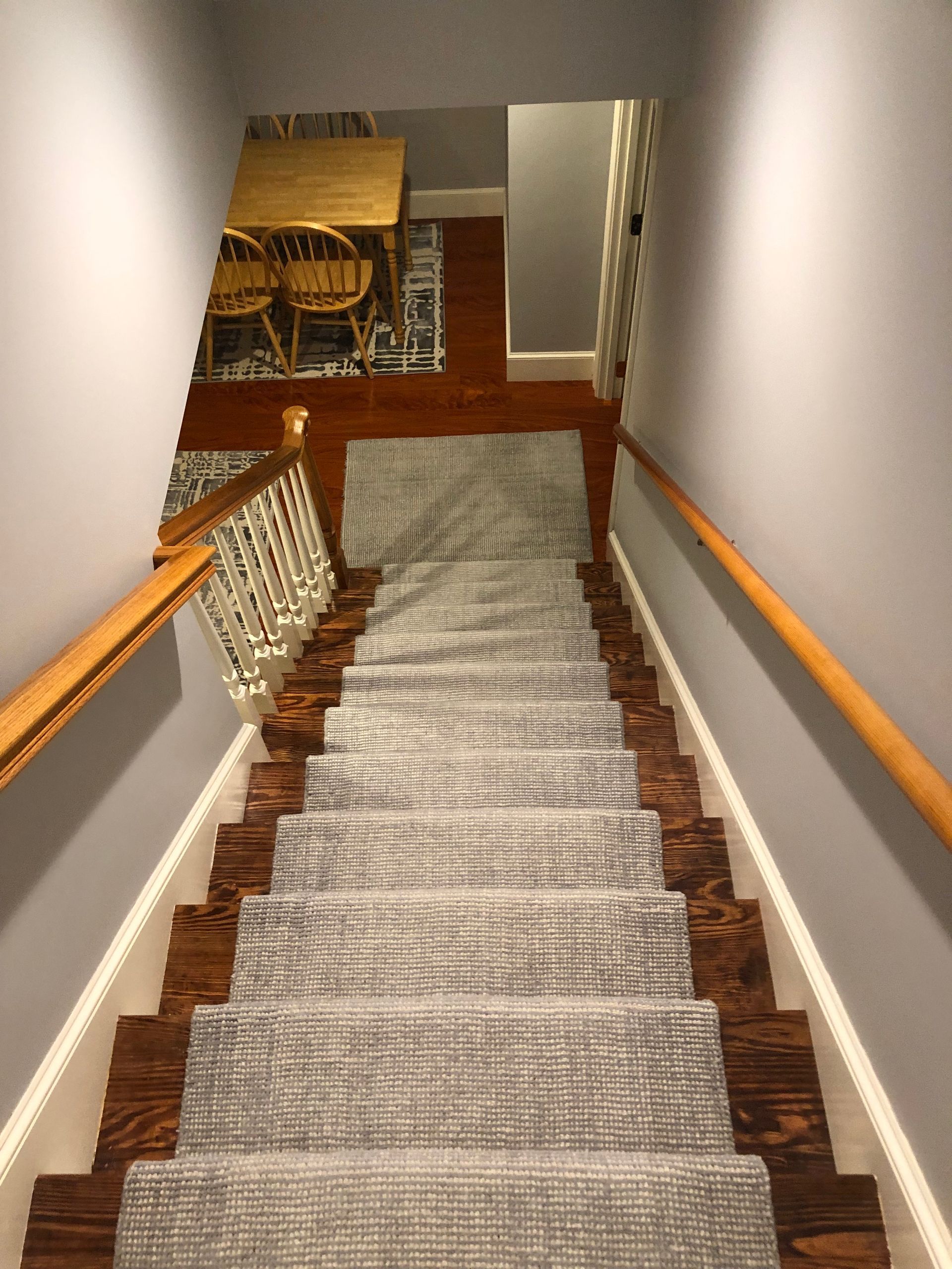 Carpeted staircase with wooden handrails and gray walls, leading down to a lower hallway.