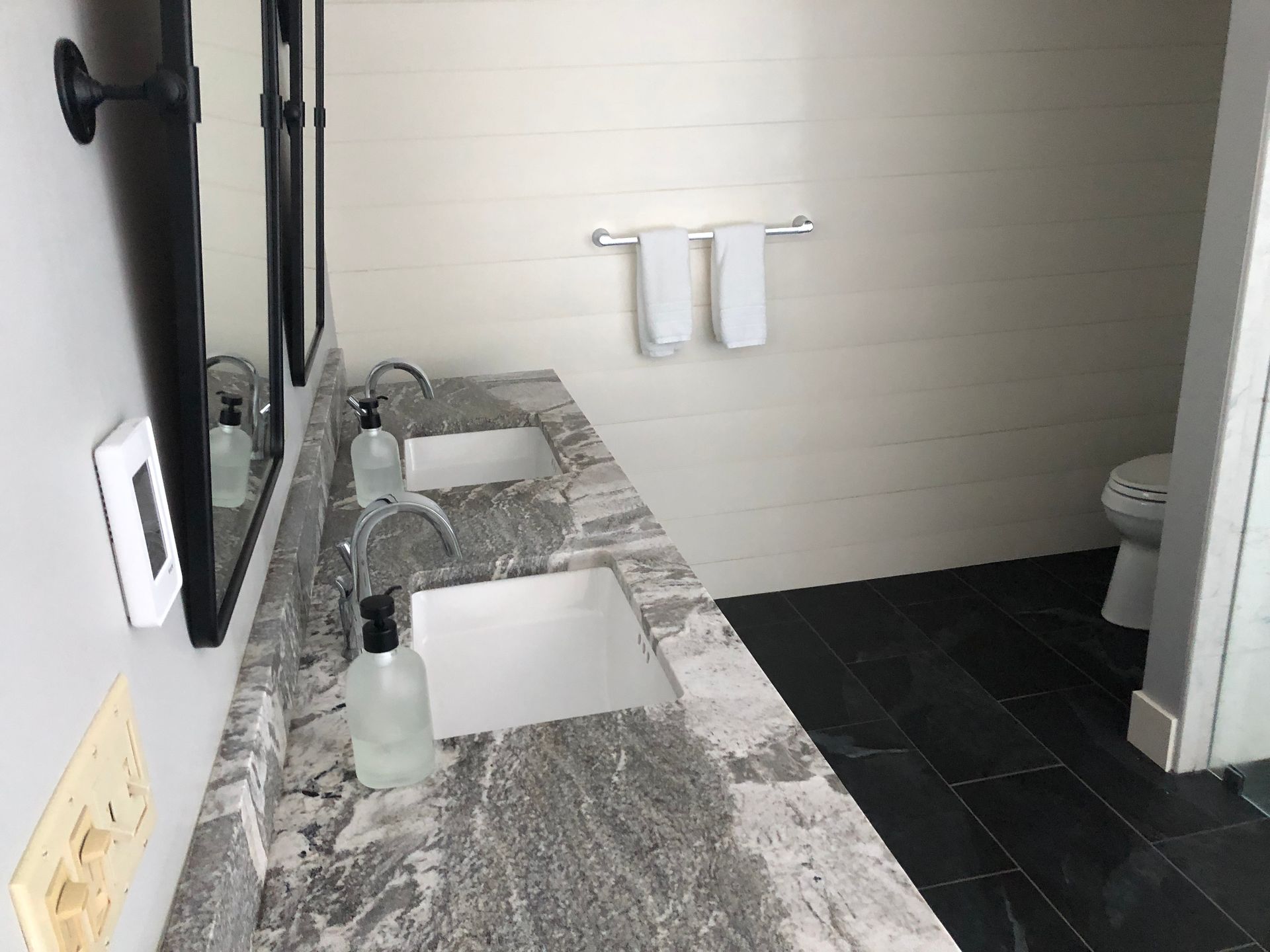 Modern bathroom vanity with gray marble countertop, sink, soap dispensers, mirror, and black tile floor