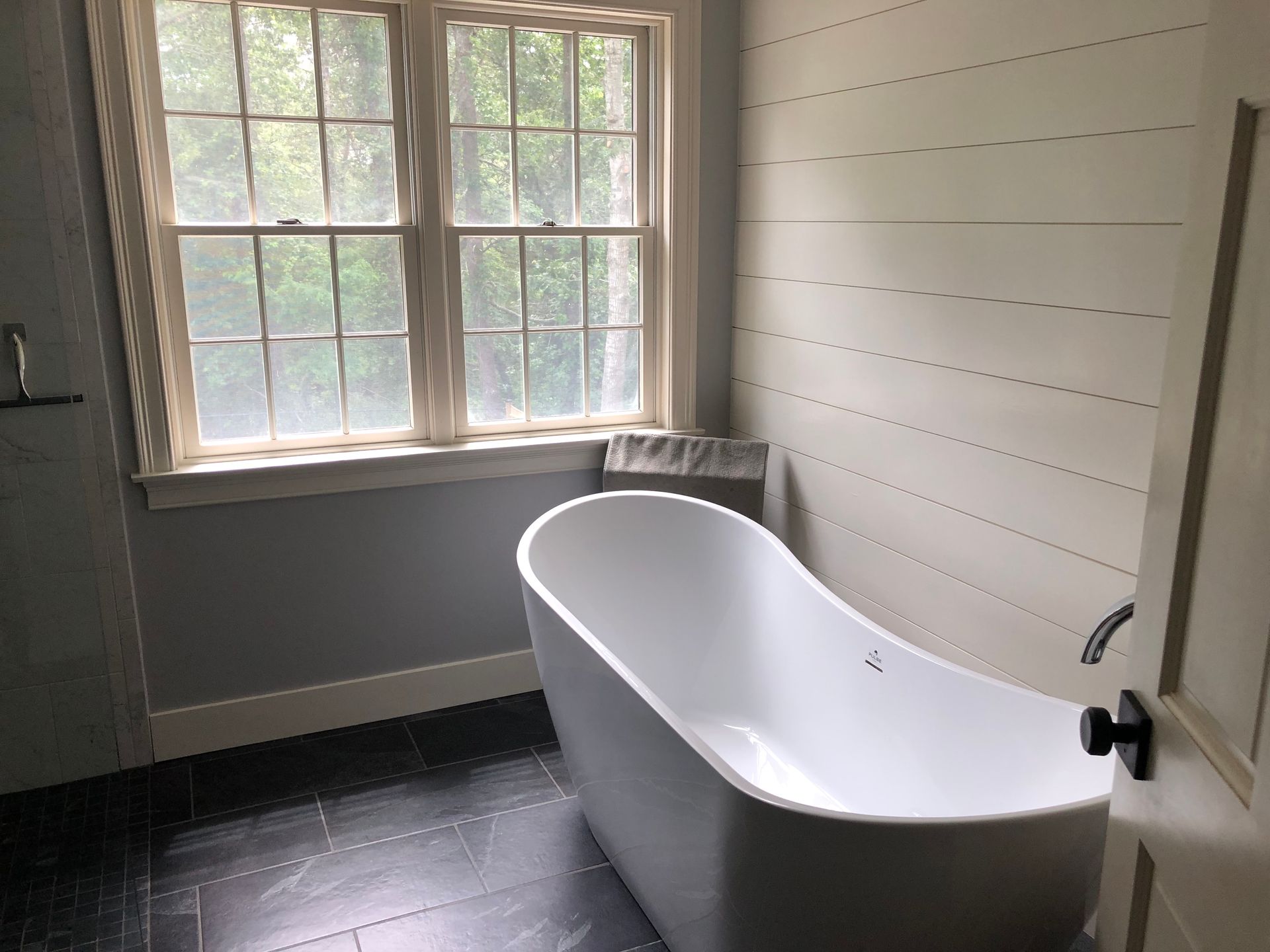 Empty bathroom with a white clawfoot tub, window, and dark floor tiles.