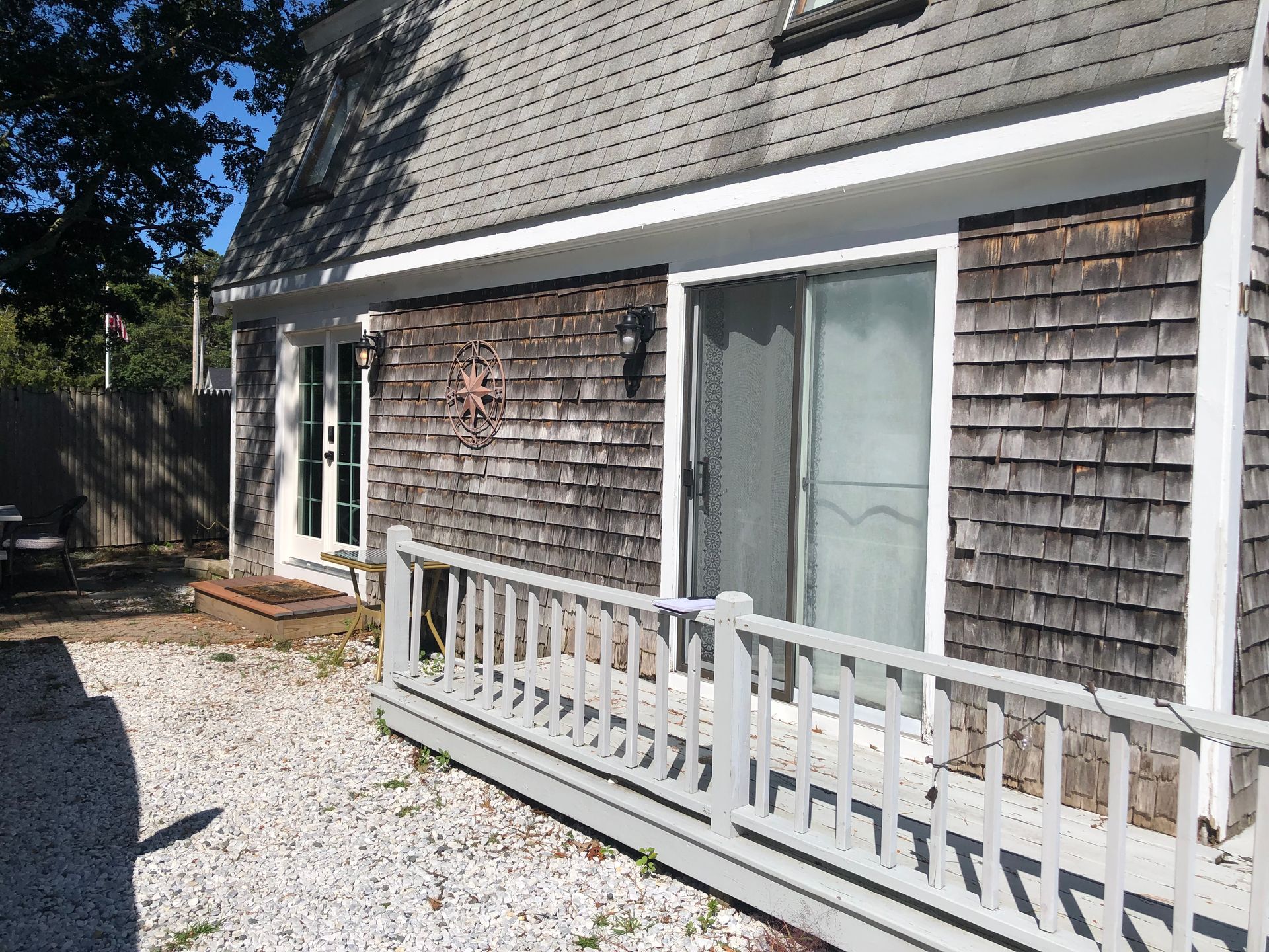 Side view of a house with gray shingle siding, white railing, sliding doors, and a gravel patio.