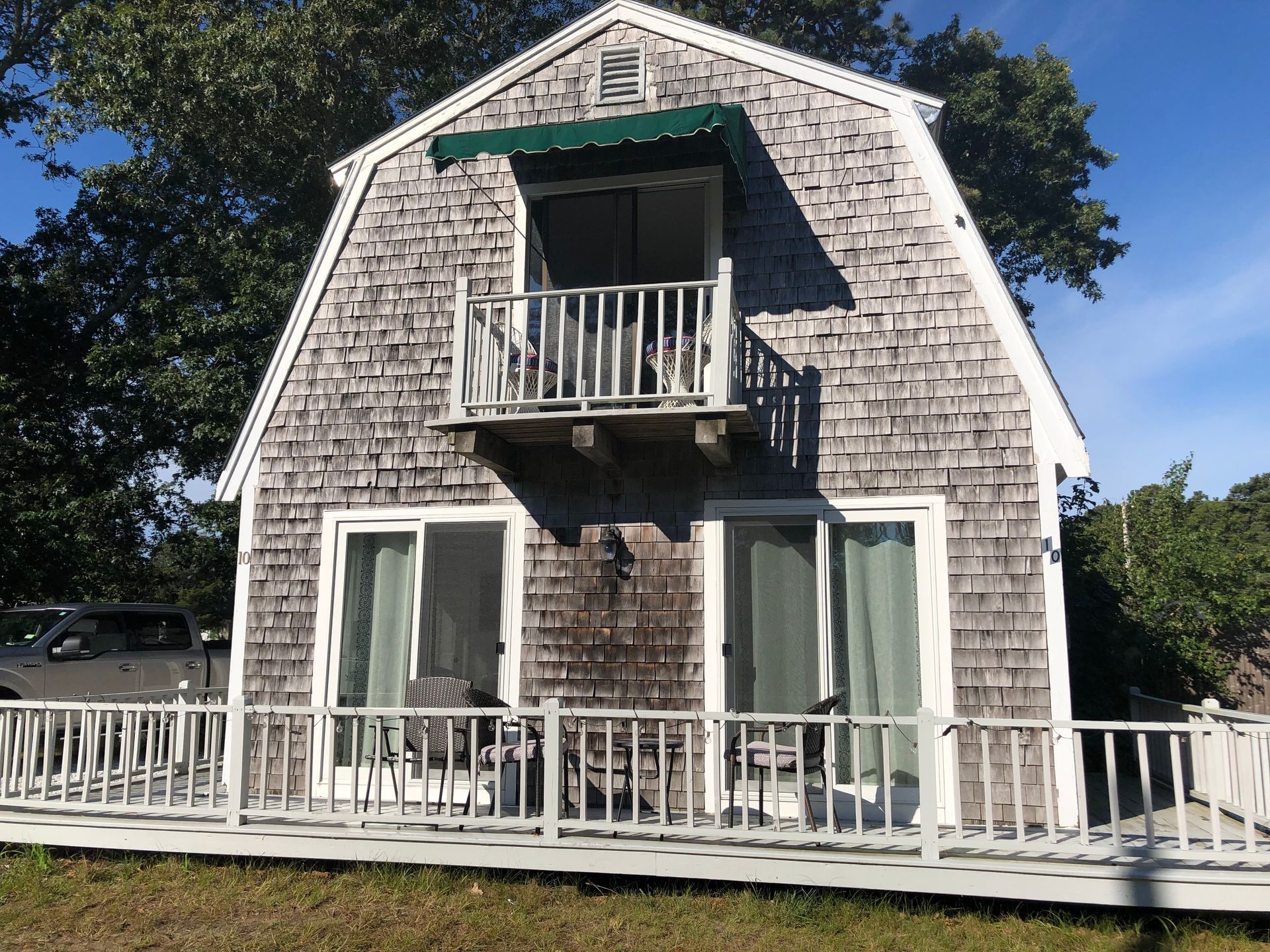 Weathered white shingle house with a small balcony and wide porch railing under a blue sky
