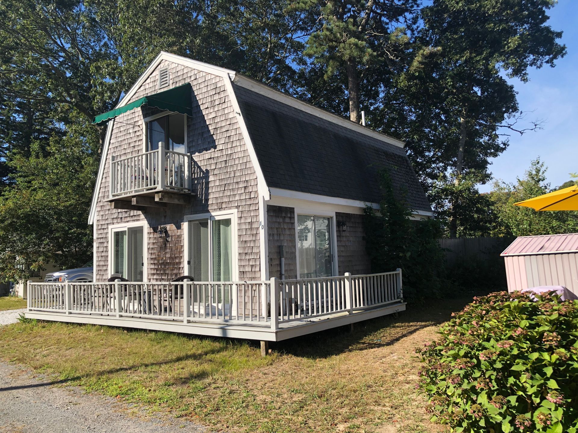 Small stone cottage with green shutters, white porch railings, and a balcony in a grassy yard.