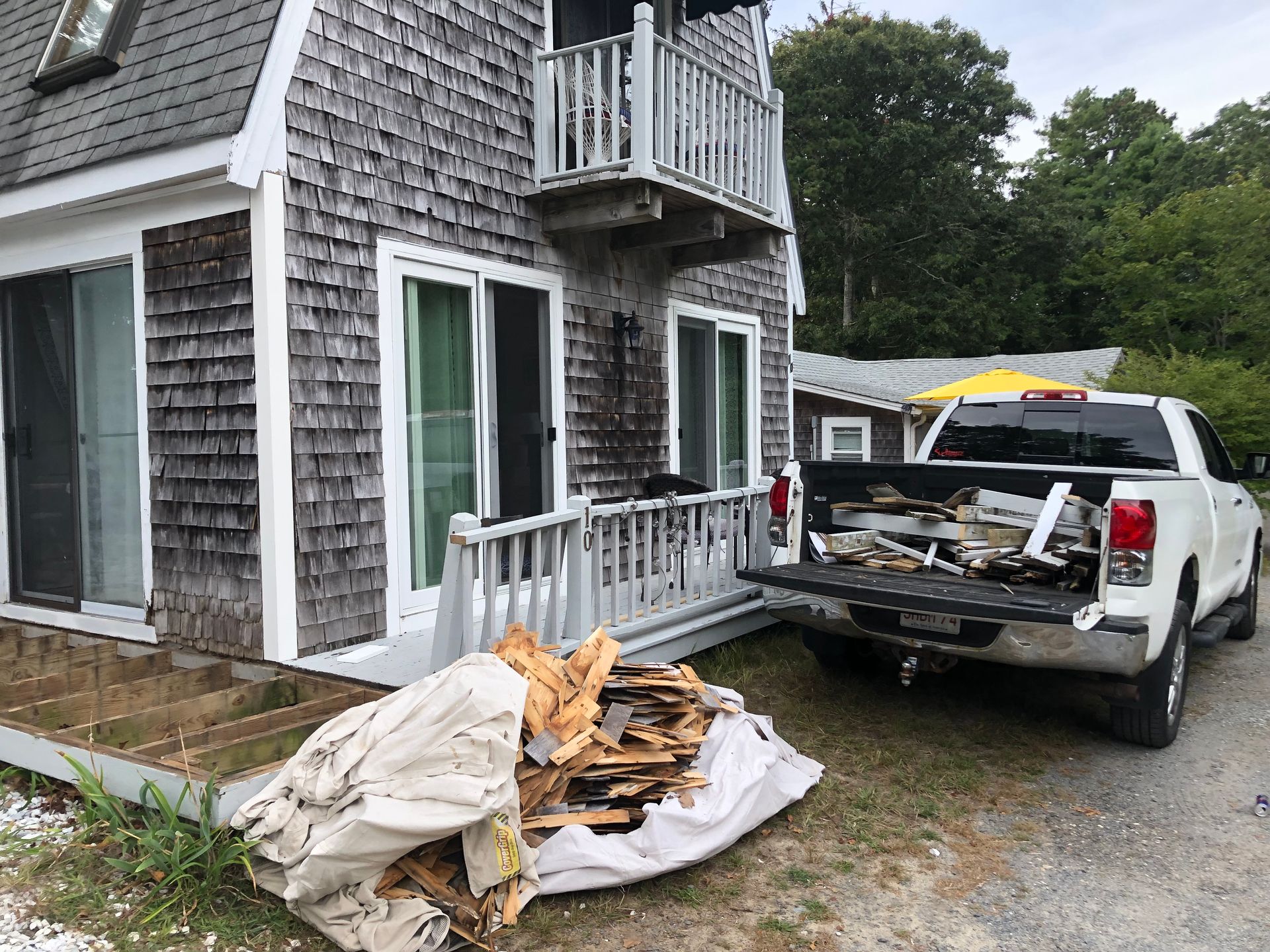 Pile of debris and construction waste beside a white house, with a pickup truck parked nearby.