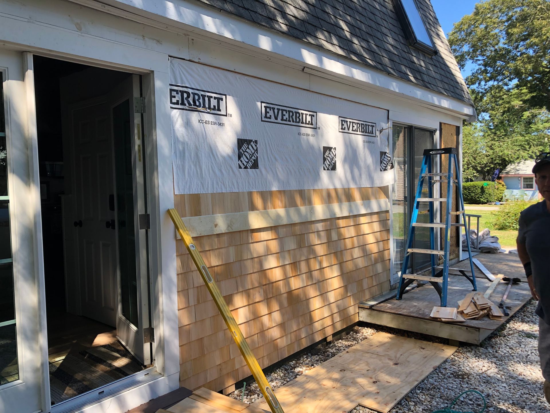 Worker installing siding on a house exterior with ladder and tools