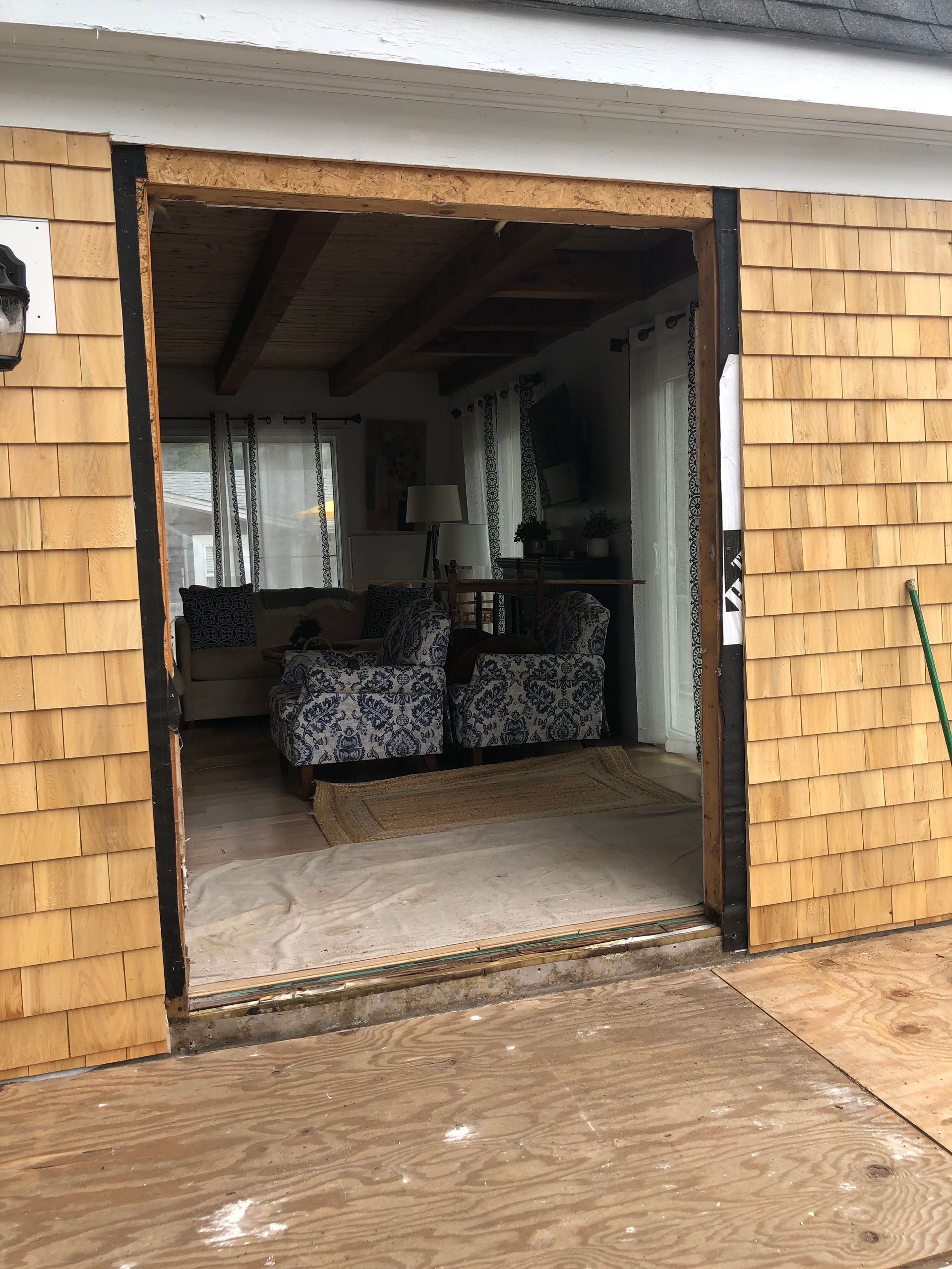 Open doorway to a rustic living room with two patterned armchairs and a wet wooden deck outside