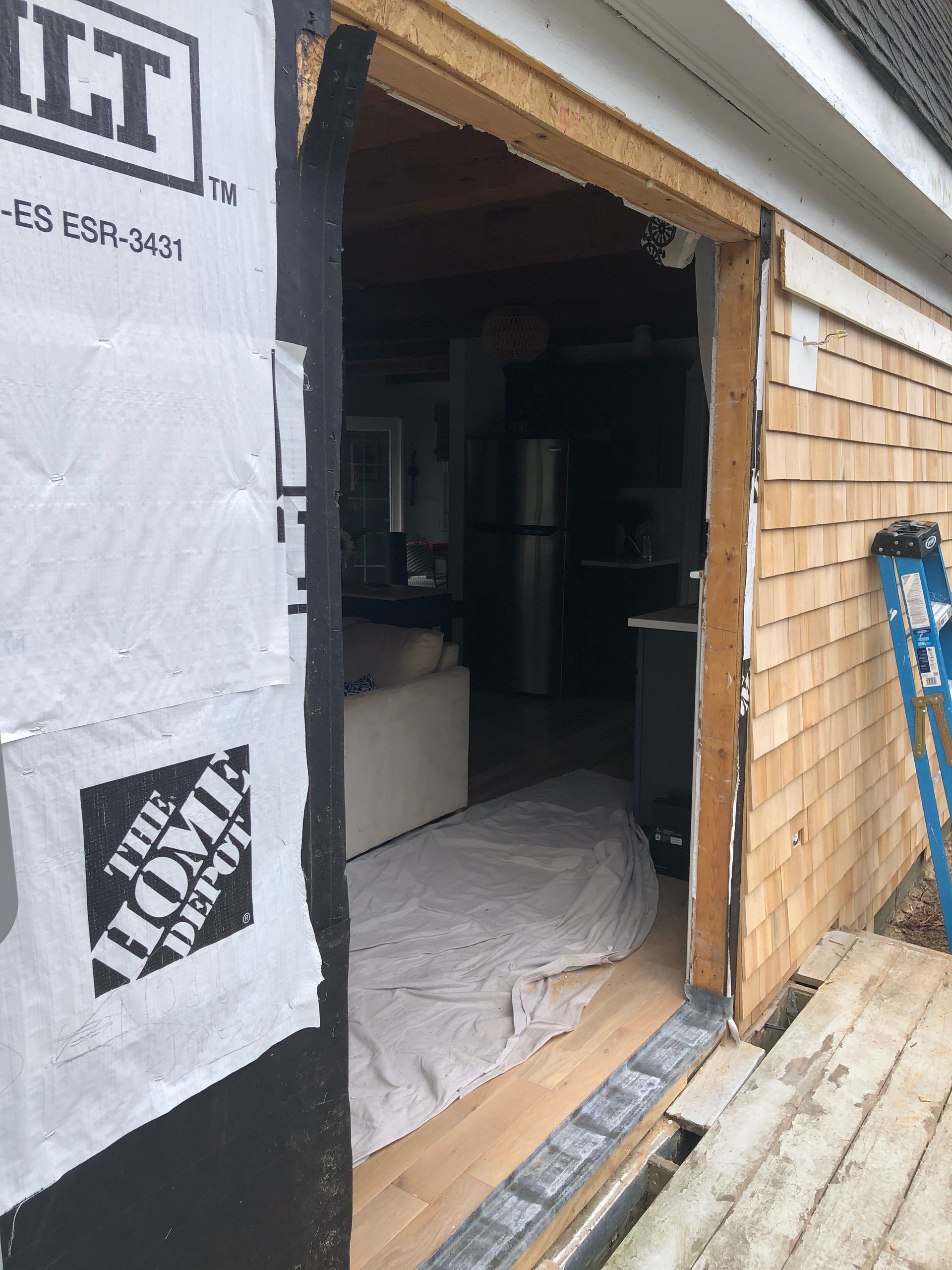 Partially finished doorway with exposed wood framing, house wrap, and construction materials inside