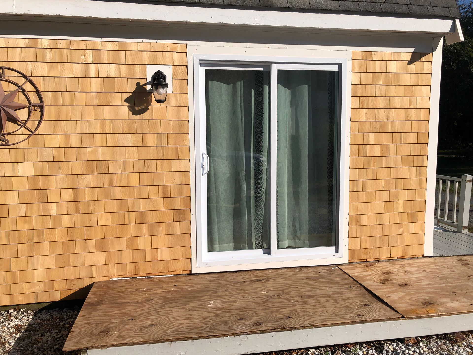 Sliding glass doors on a house exterior with wood shingle siding and a small patio mat