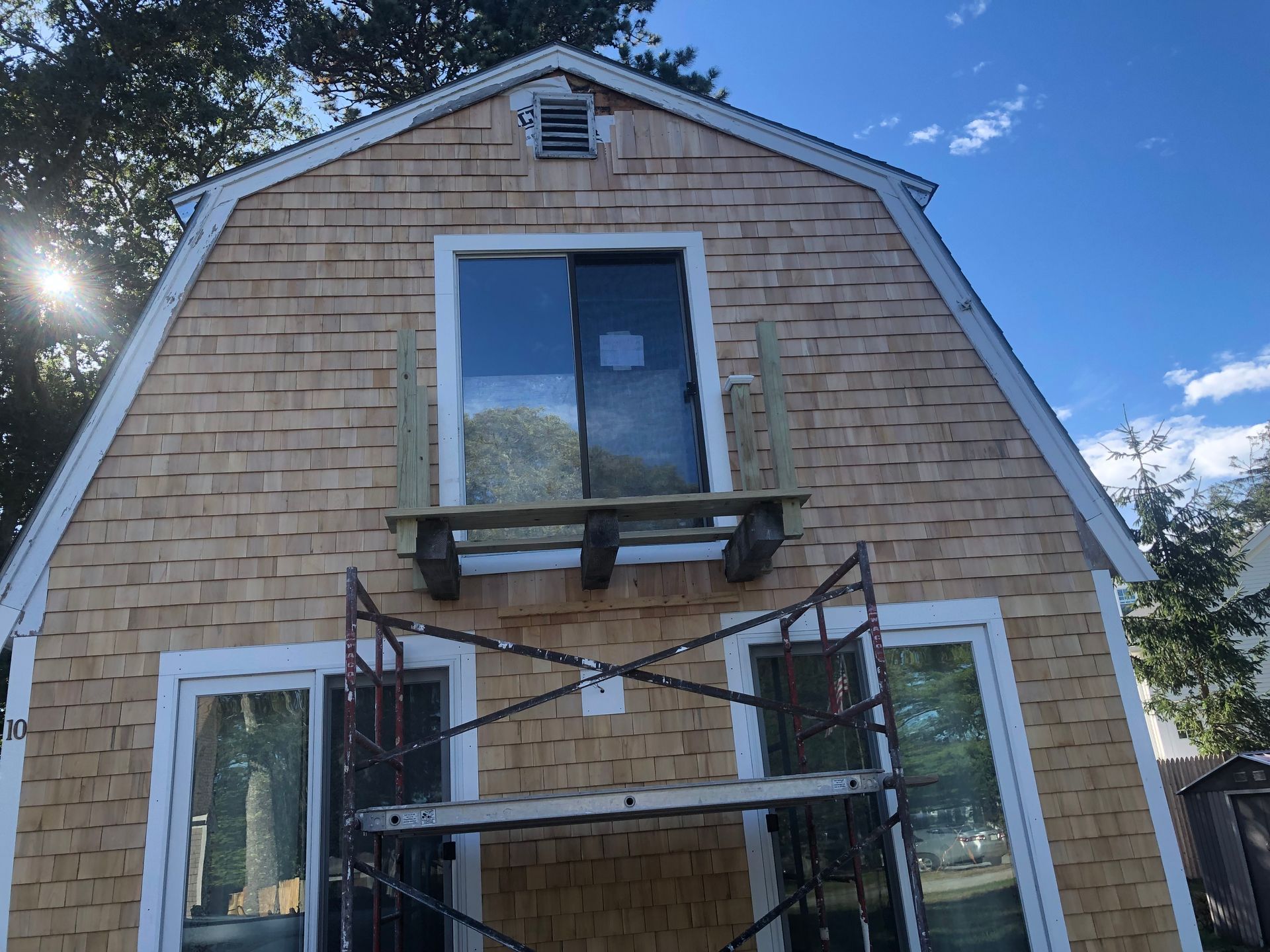 Front view of a house with tan siding, a central window, and scaffolding over the entrance.