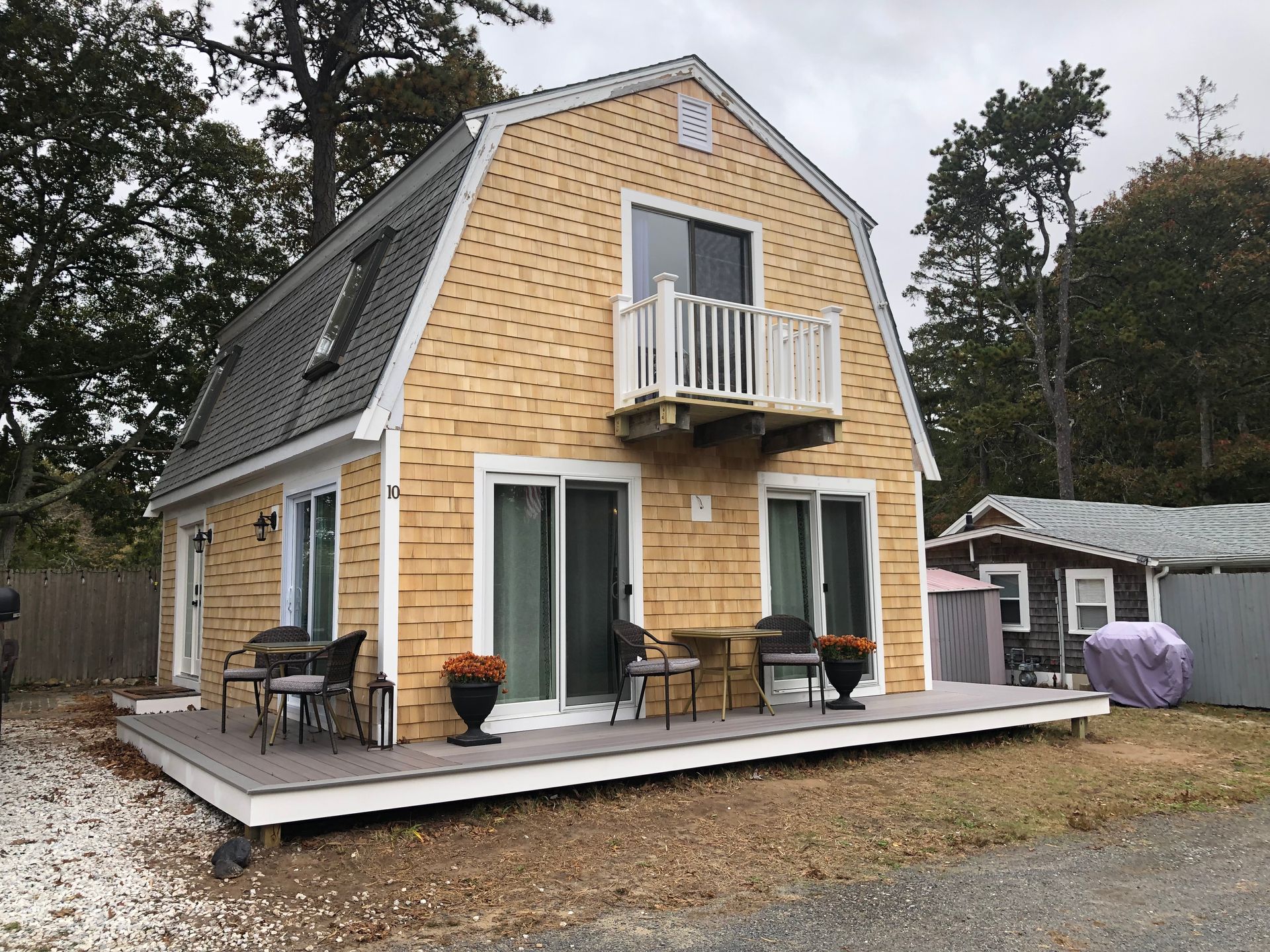 Two-story brick house with a small balcony and a raised deck in a wooded yard