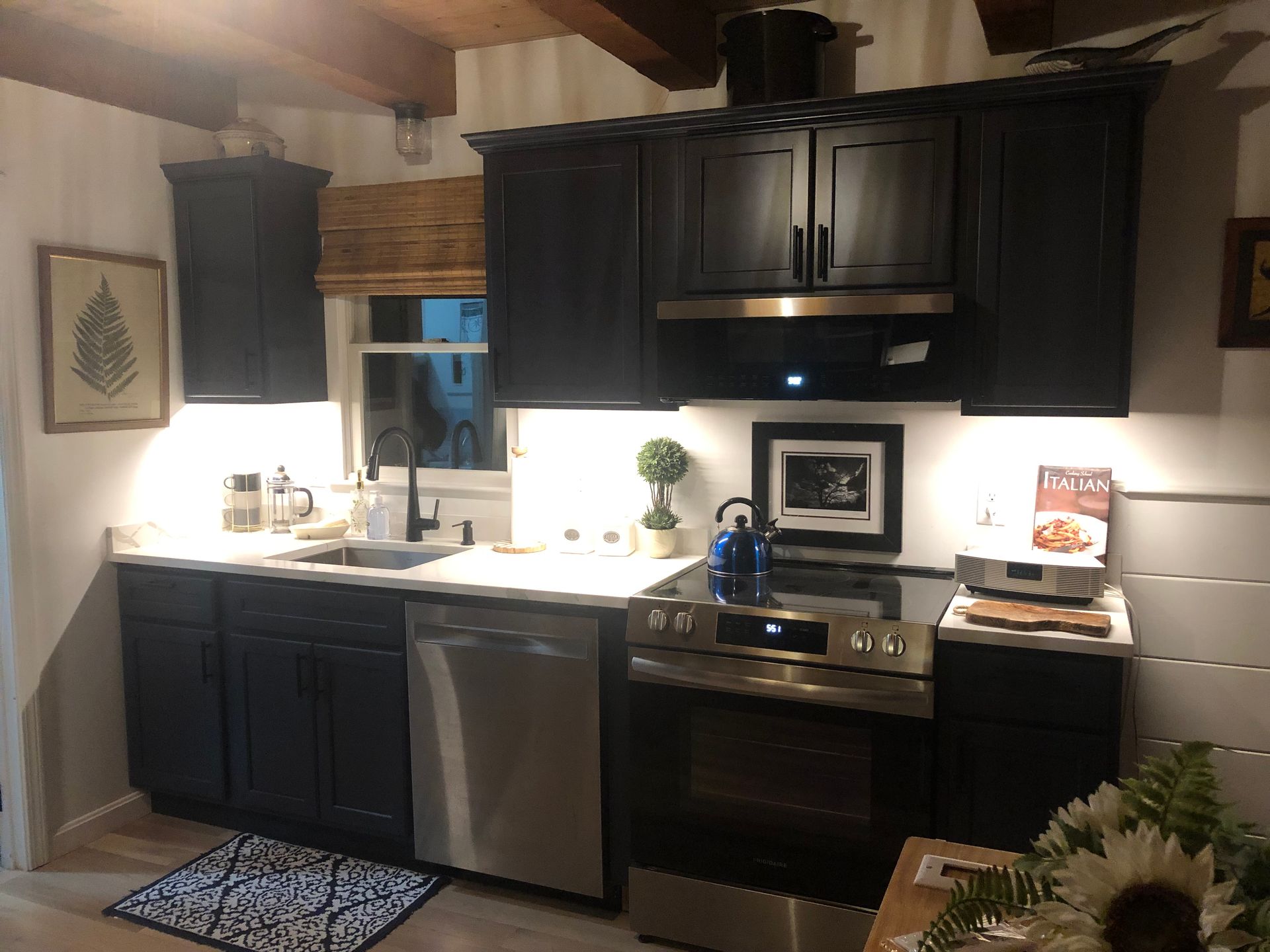 Modern kitchen with black cabinets, white countertops, stainless steel appliances, and warm lighting