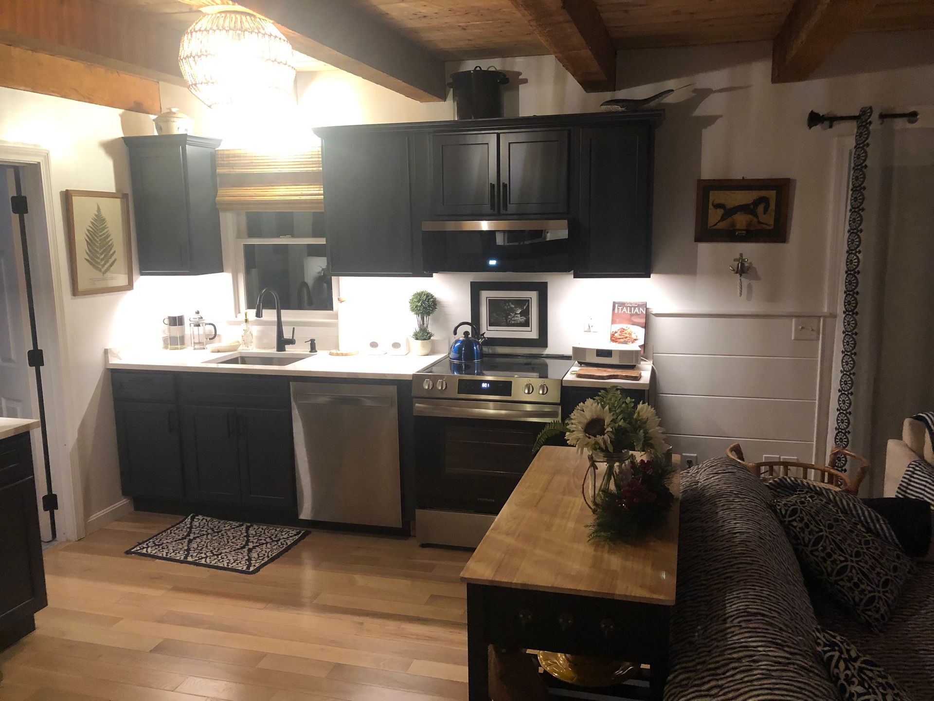 Cozy kitchen with dark cabinets, stainless appliances, wood table, and warm overhead lighting
