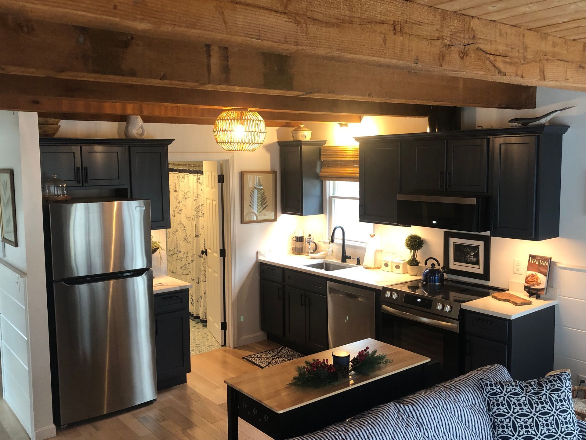 Compact kitchen with dark cabinets, stainless fridge, wood-beam ceiling, and a small island.