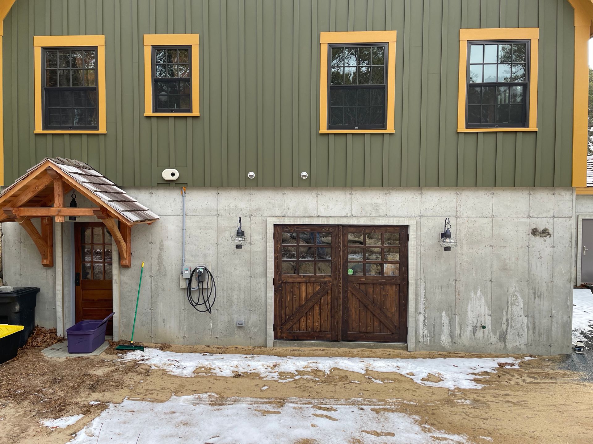 Two-story building with green upper siding, gray lower wall, wooden door, and snow on the ground