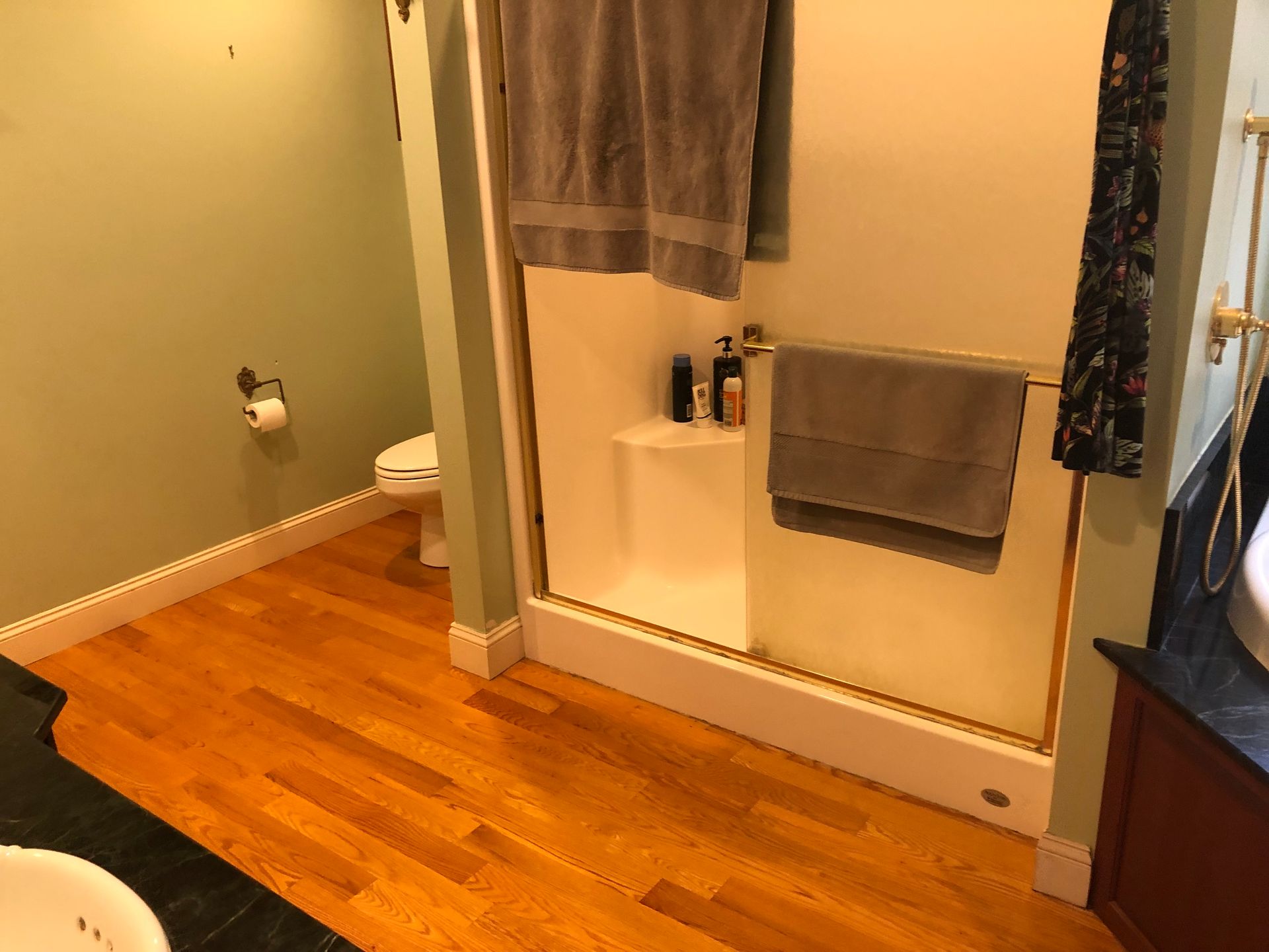 Bathroom with wood floor, shower curtain, towel, and gray bath mat beside a tub.